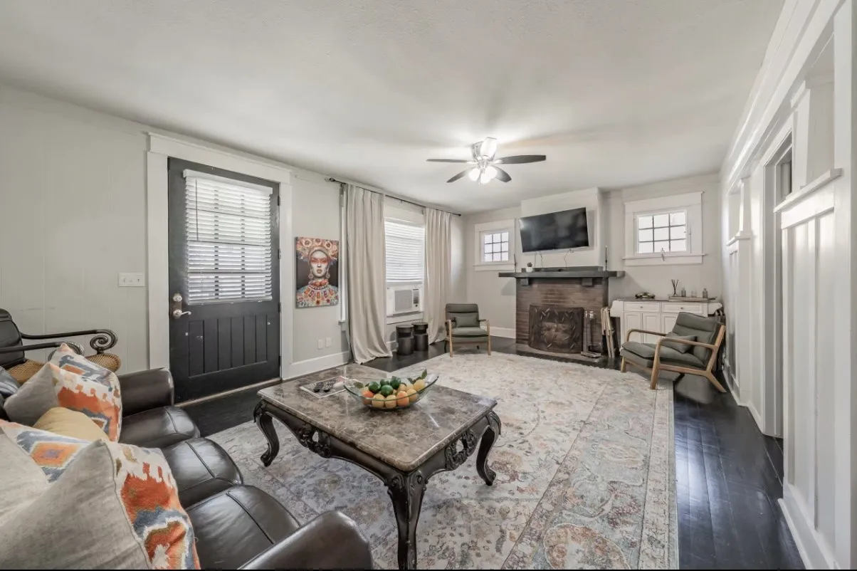 Expansive living area with dark wood-finish flooring, a decorative fireplace, and a ceiling fan