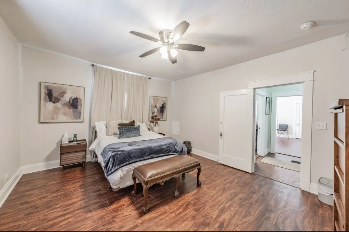 Spacious room featuring rich wood-finish flooring, a ceiling fan with integrated lighting, and white baseboards