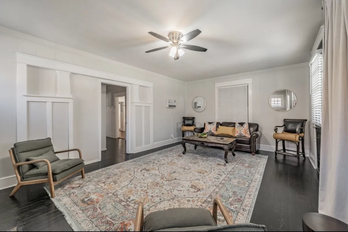 Spacious living area featuring dark wood-finish flooring, a ceiling fan with integrated lighting, and white baseboards