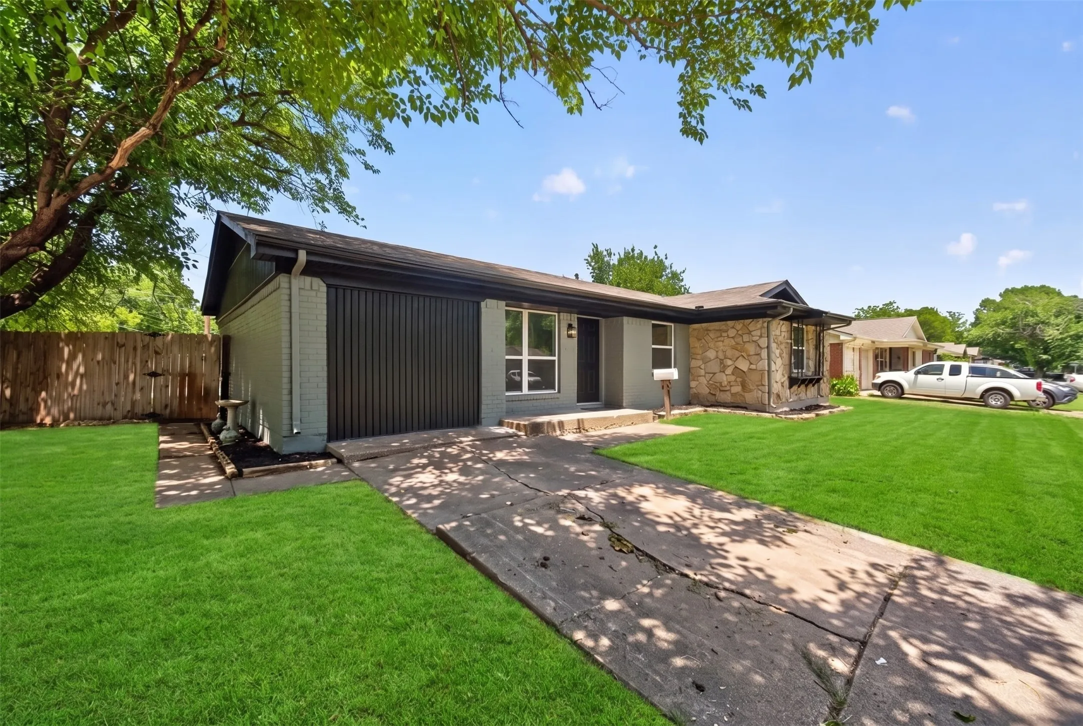 Gray brick exterior with stone accent facade, featuring a front lawn, paved driveway, and mature tree