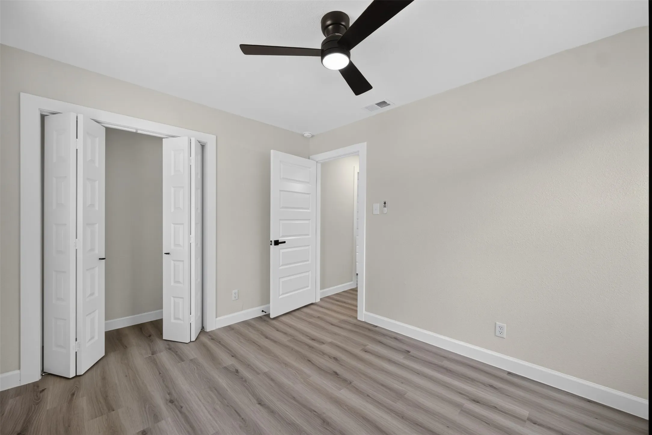 Spacious room featuring wood-finish flooring, light neutral wall tones, and a modern ceiling fan