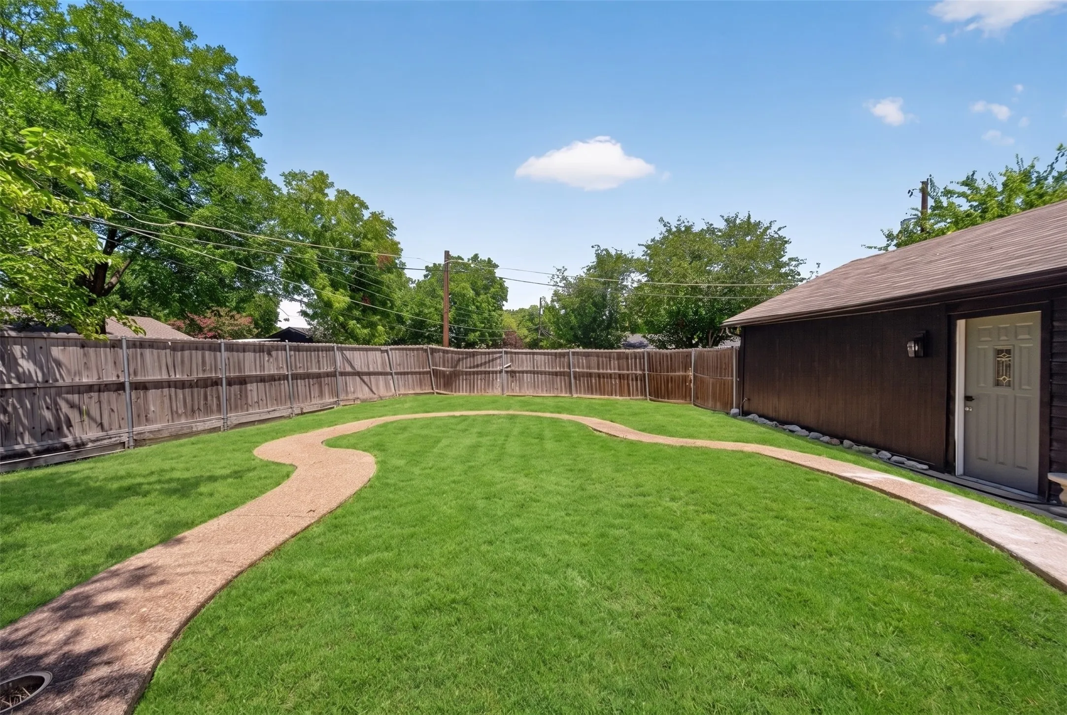 Spacious backyard featuring a curved gravel path, expansive lawn, wood privacy fencing, and a detached structure with a white entry door