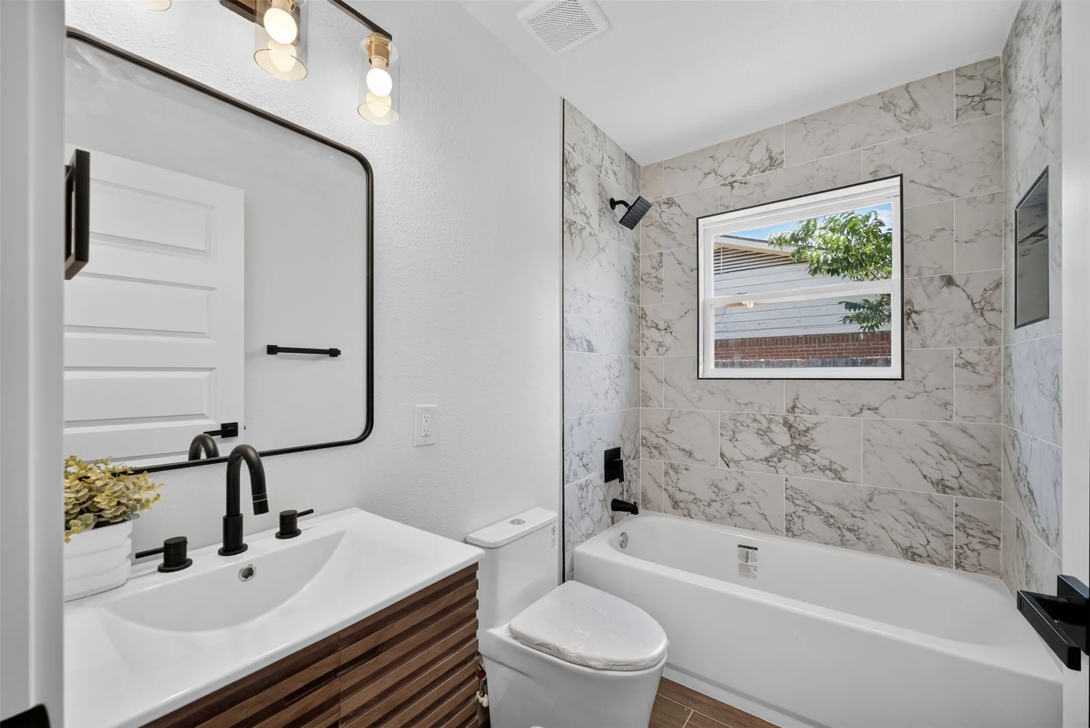 Full bathroom featuring a wood-finish vanity with an integrated sink, matte black fixtures, and a rectangular mirror