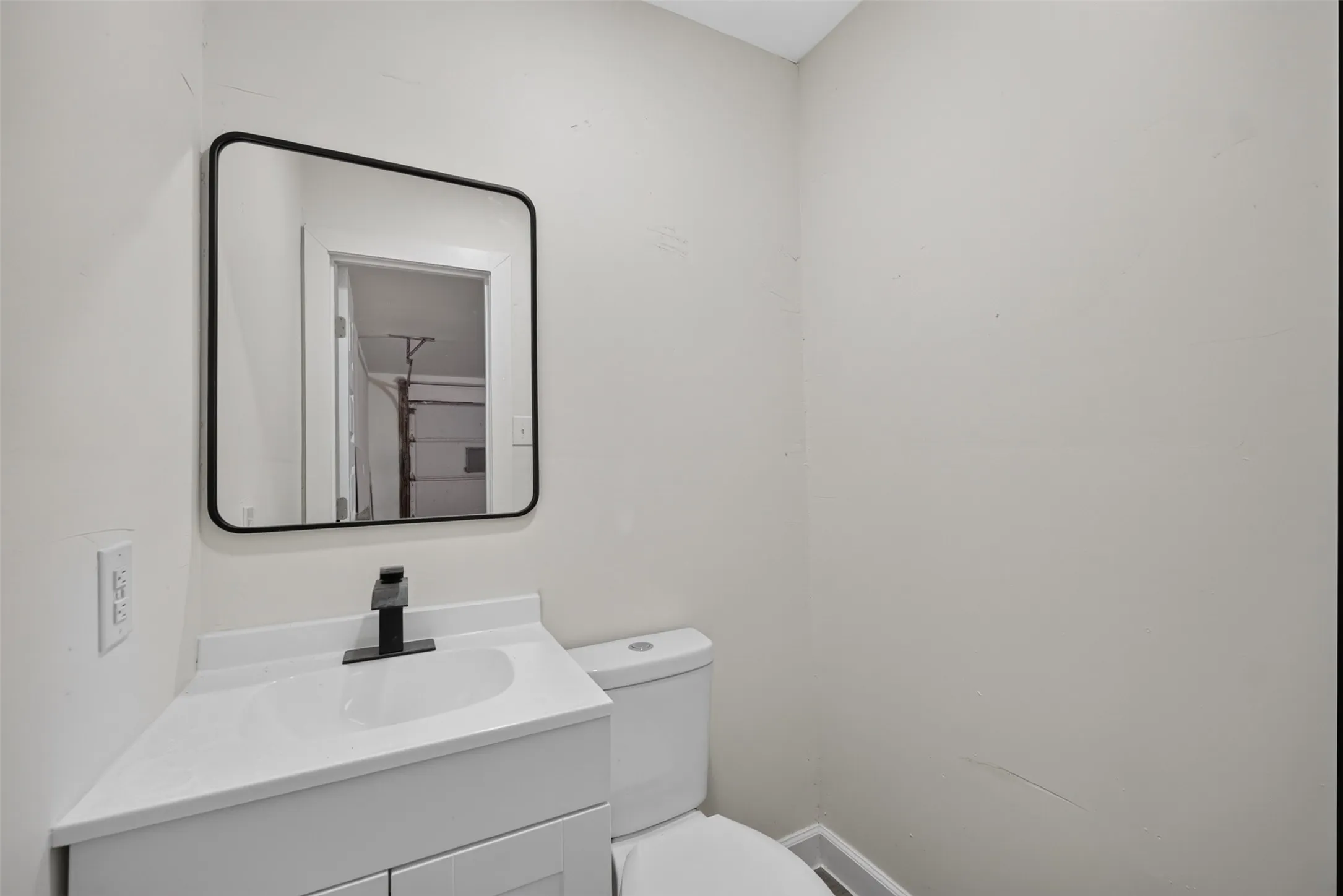 Bathroom featuring a white vanity with an integrated sink, a matte black faucet, and a black-framed rectangular mirror