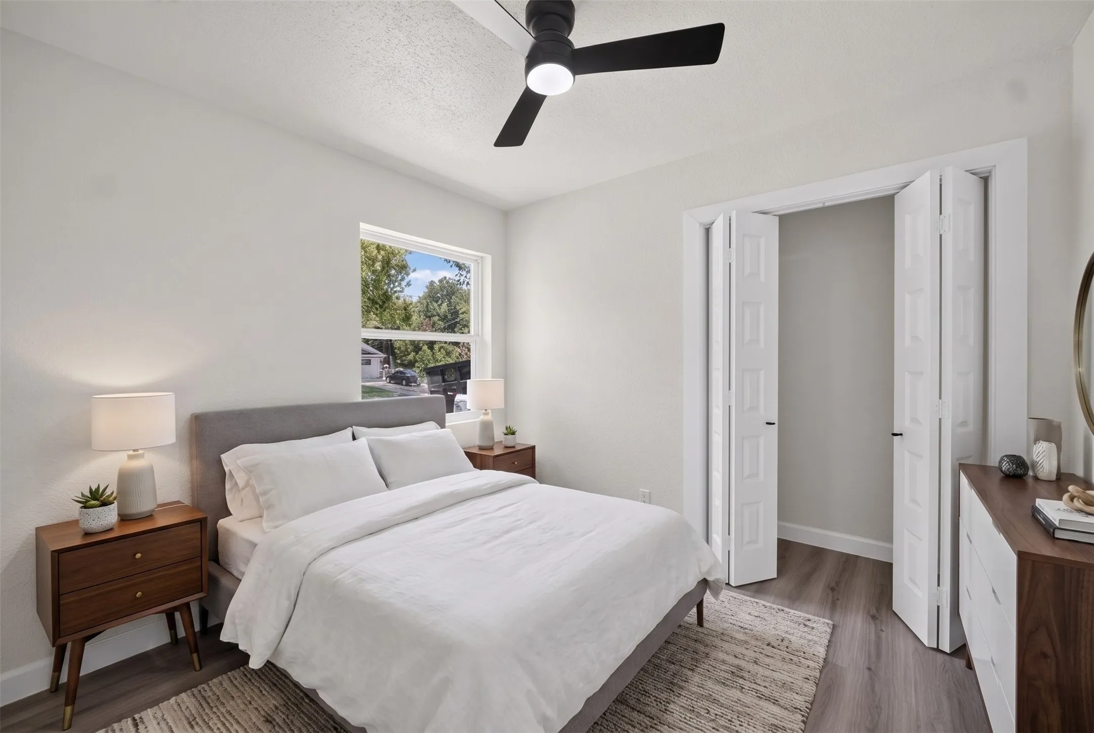 Bright bedroom featuring a large window, a modern black ceiling fan, and wood-finish flooring