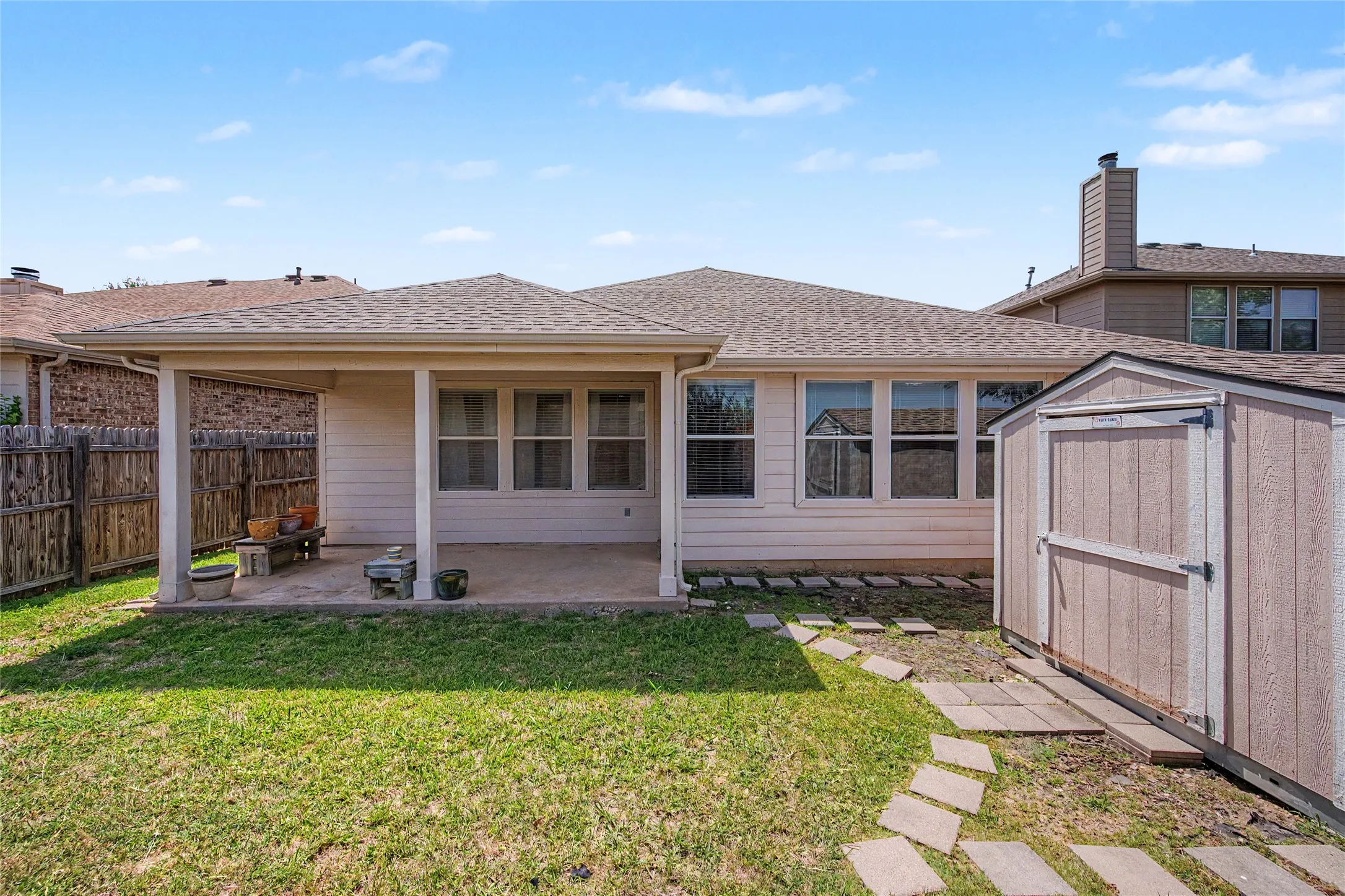 Expansive backyard featuring a covered patio with concrete flooring, multiple windows providing natural light, a wood fence, and an outdoor storage shed
