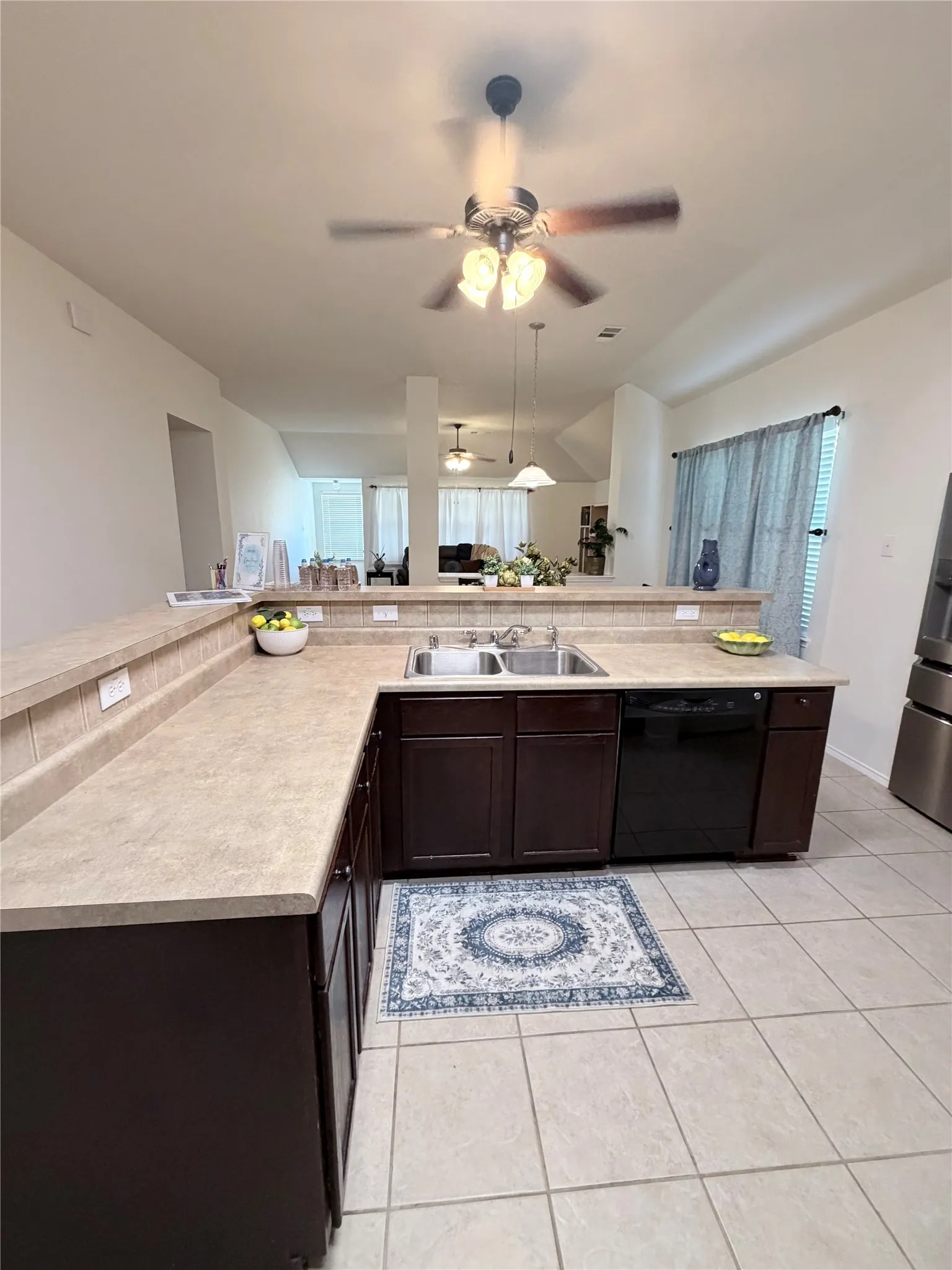 Kitchen featuring a dual basin stainless steel sink, dark wood-finish cabinetry, a black dishwasher, and neutral-toned tile flooring