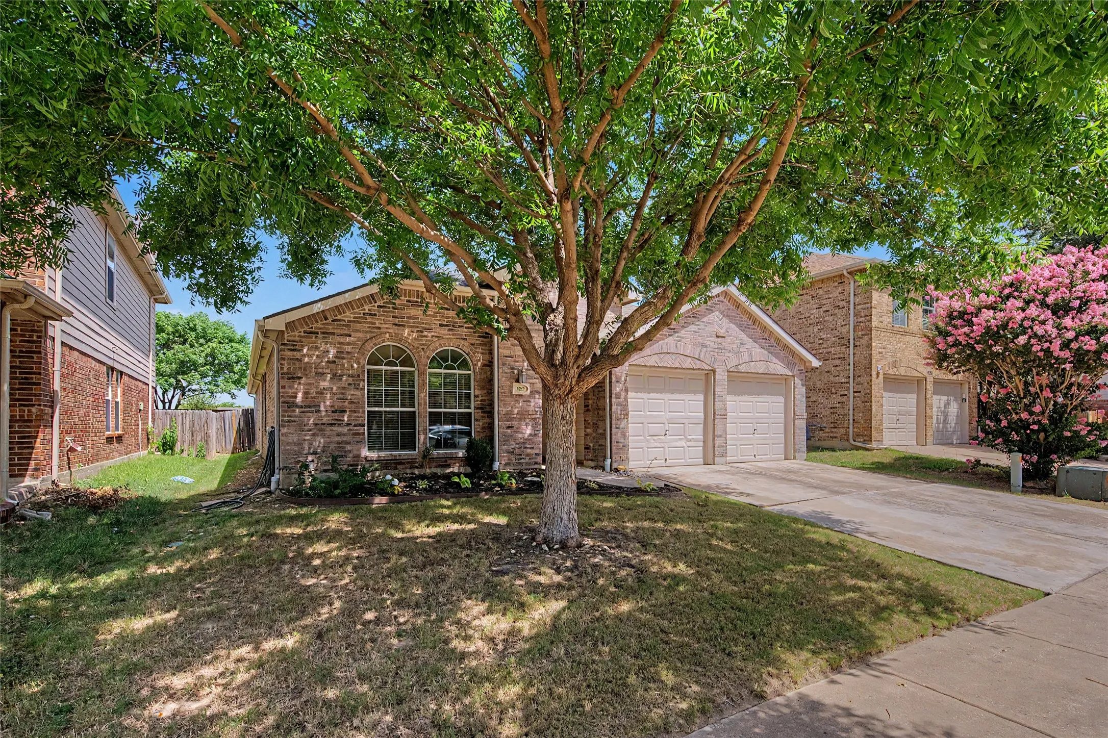 Brick and stone facade residence featuring arched windows, a two-car garage, and a mature shade tree