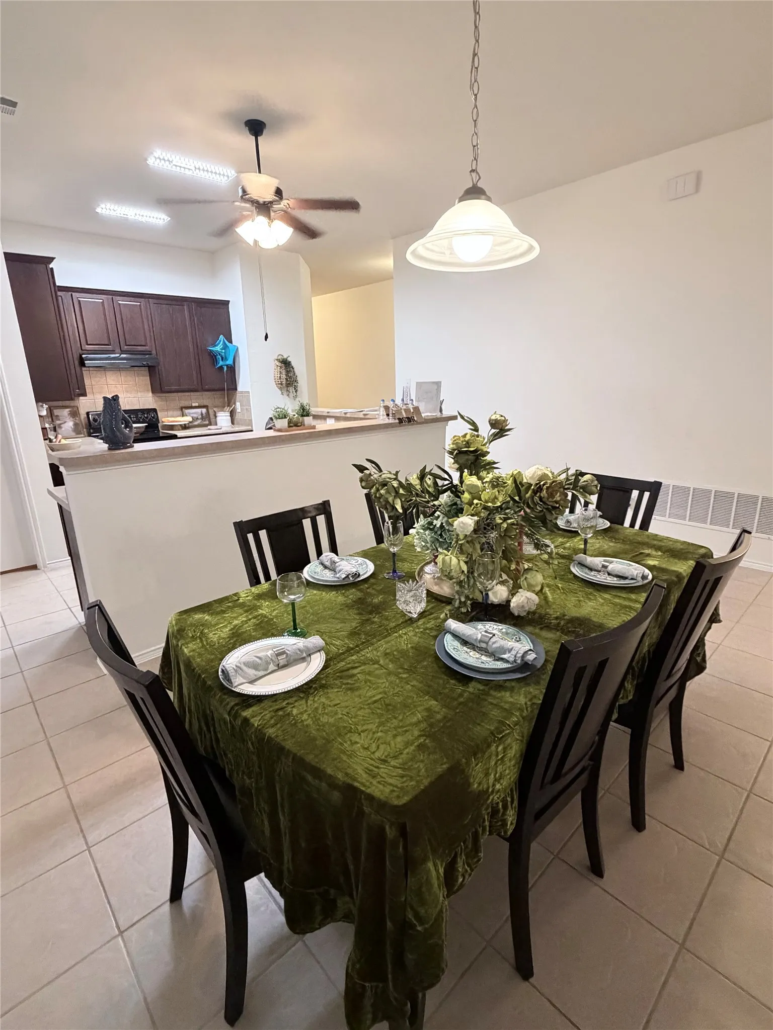Open-concept living space featuring a dining area with a pendant light fixture and a kitchen with wood-finish cabinetry, a ceiling fan, and a breakfast bar