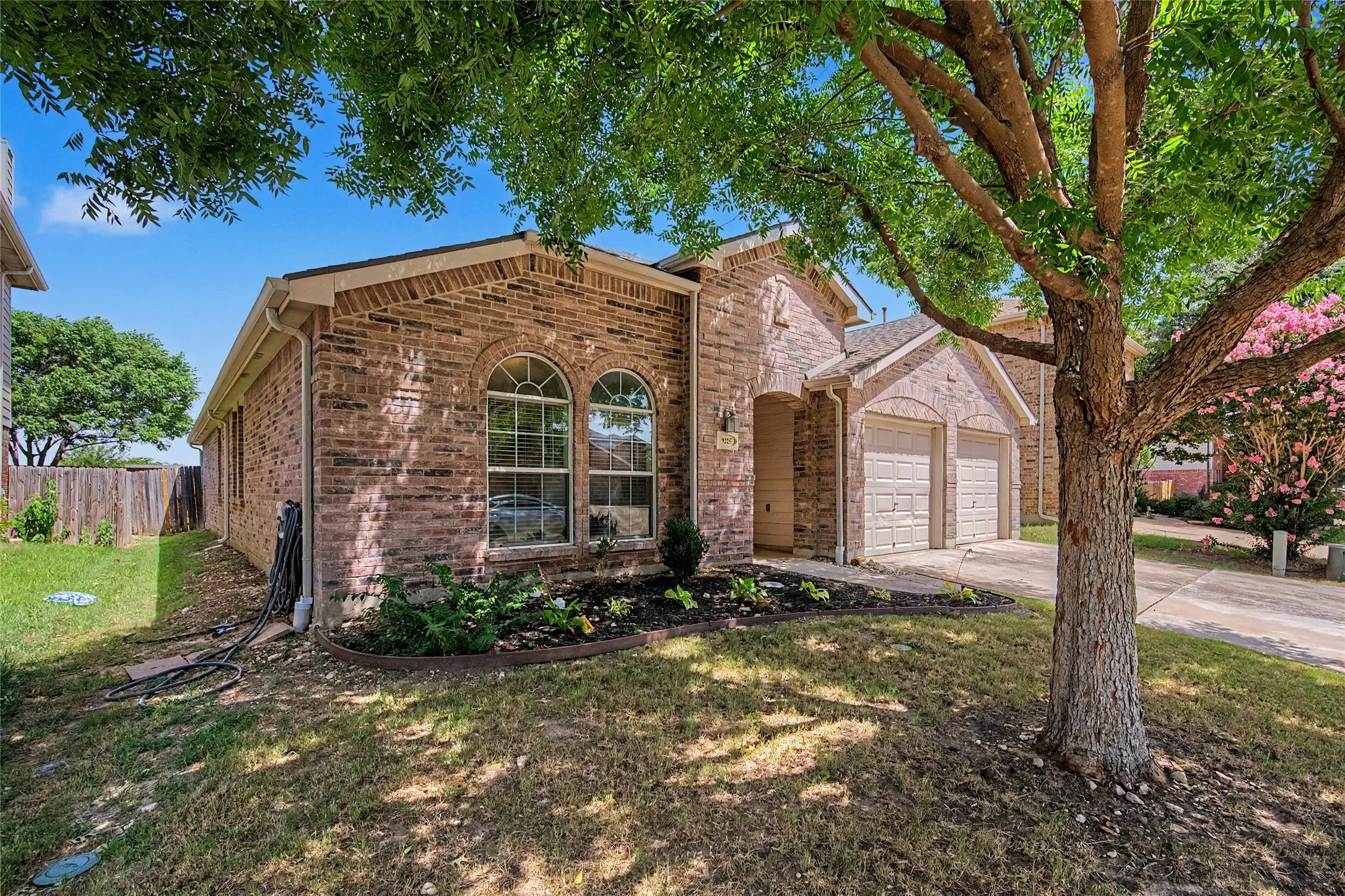 Traditional brick exterior featuring a two-car garage, arched window accents, and a landscaped front garden bed