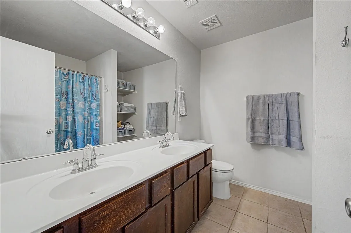 Bathroom featuring a double vanity with integrated sinks, wood-finish cabinetry, and a large wall-mounted mirror