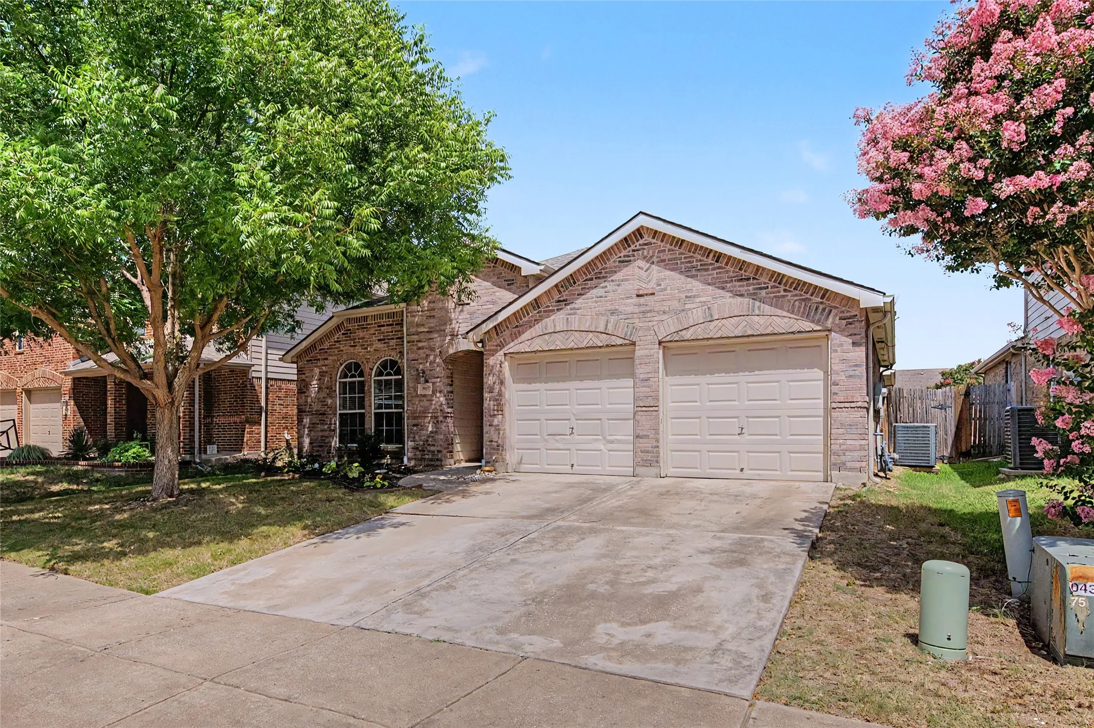 Brick exterior featuring a two-car garage with arched lintels, a concrete driveway, and mature landscaping