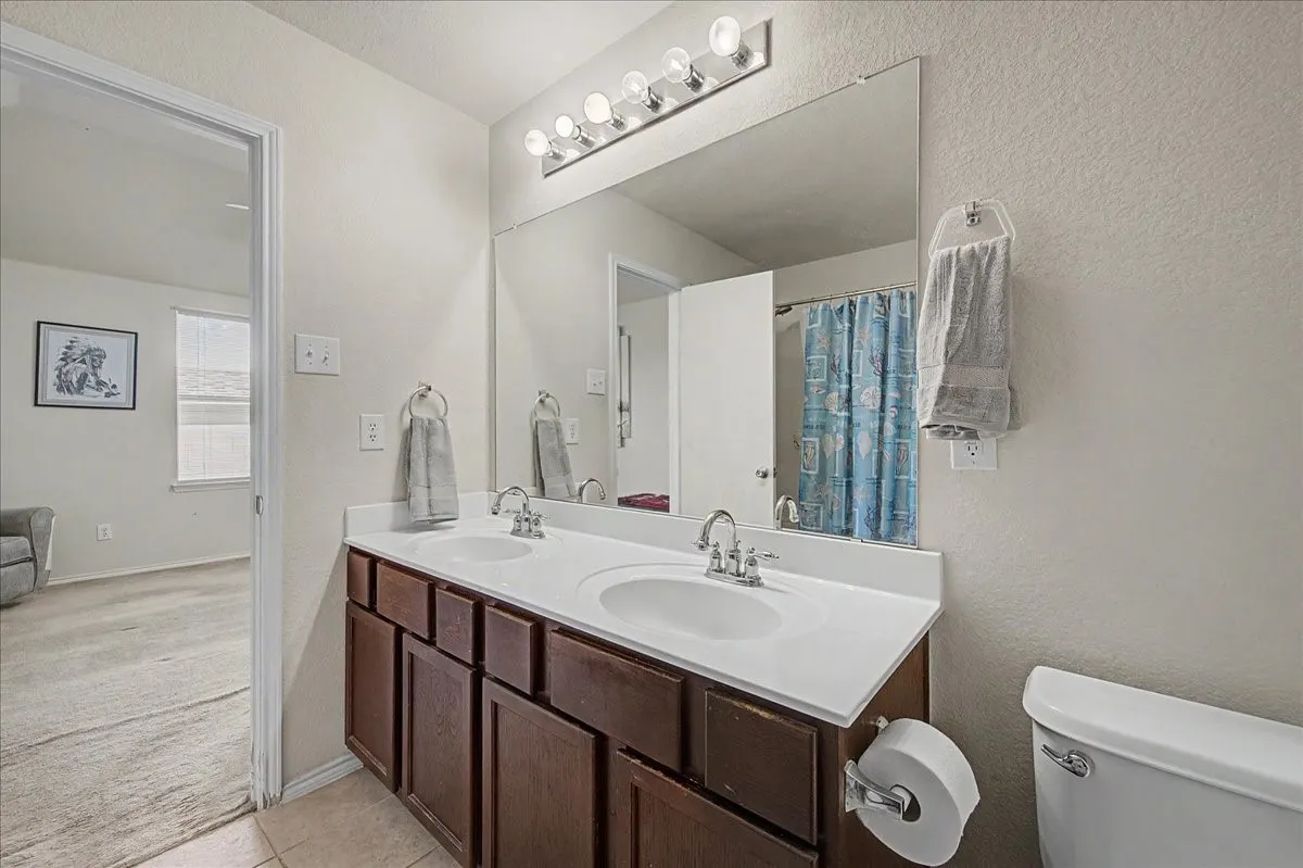 Bathroom featuring a dual vanity with a white countertop and wood-finish cabinetry, a large mirror, and overhead vanity lighting