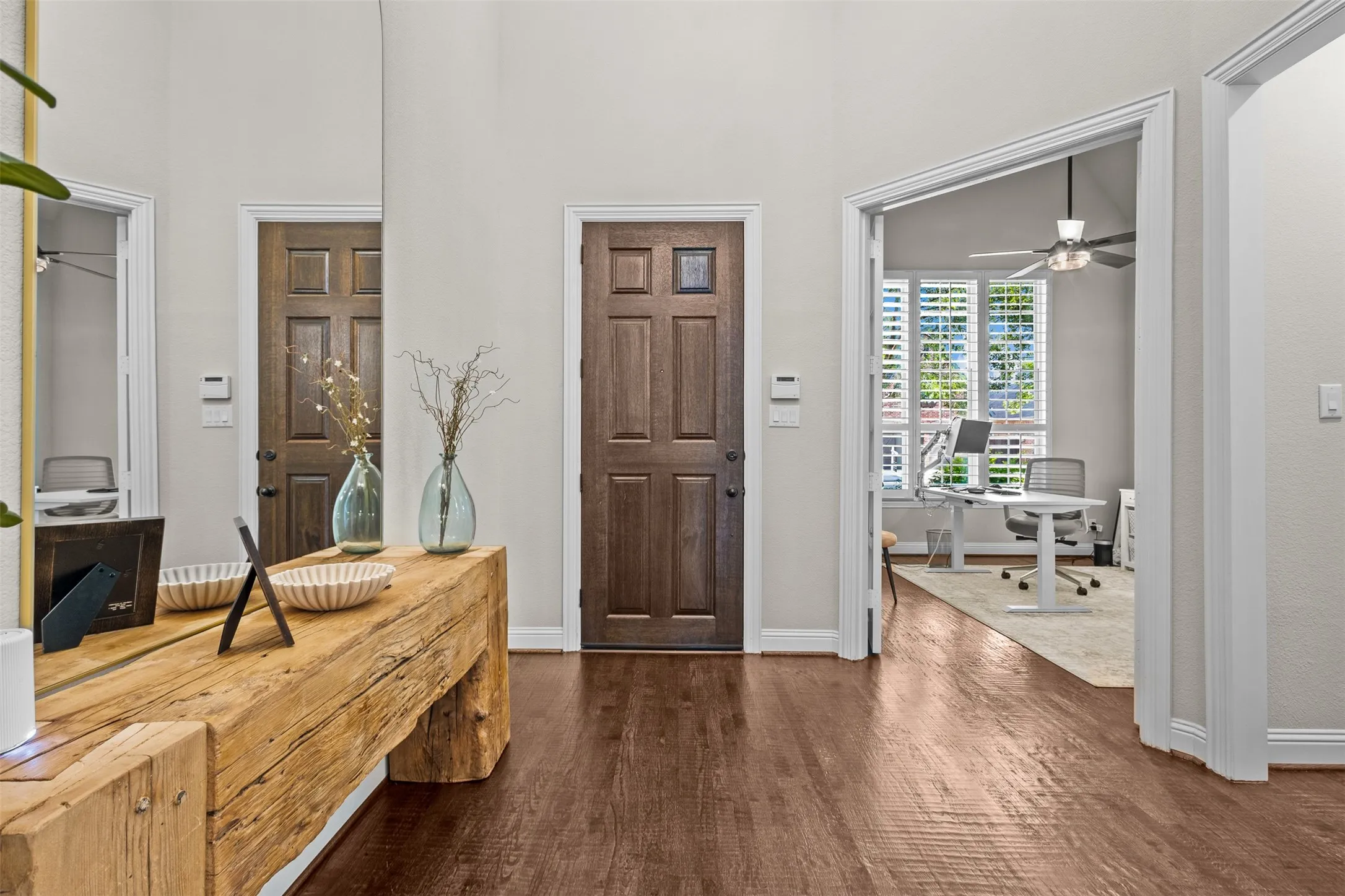 Entryway featuring wood-finish flooring, a paneled door with glass insert, high ceilings, and an open doorway leading to a room with plantation shutters and a ceiling fan