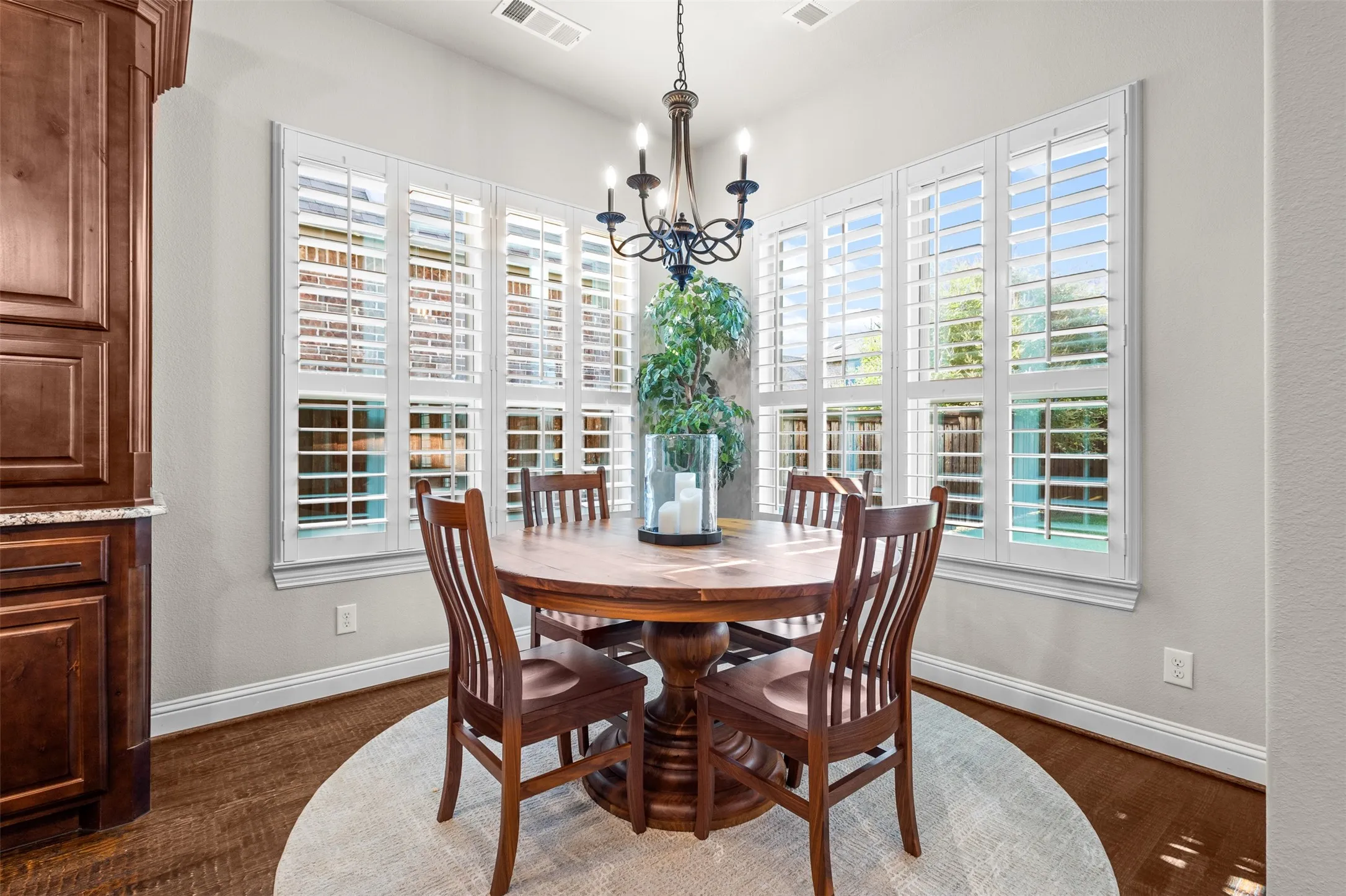 Dining area featuring a bay window with plantation shutters, wood-finish flooring, a wrought iron chandelier, and built-in cabinetry with a granite countertop