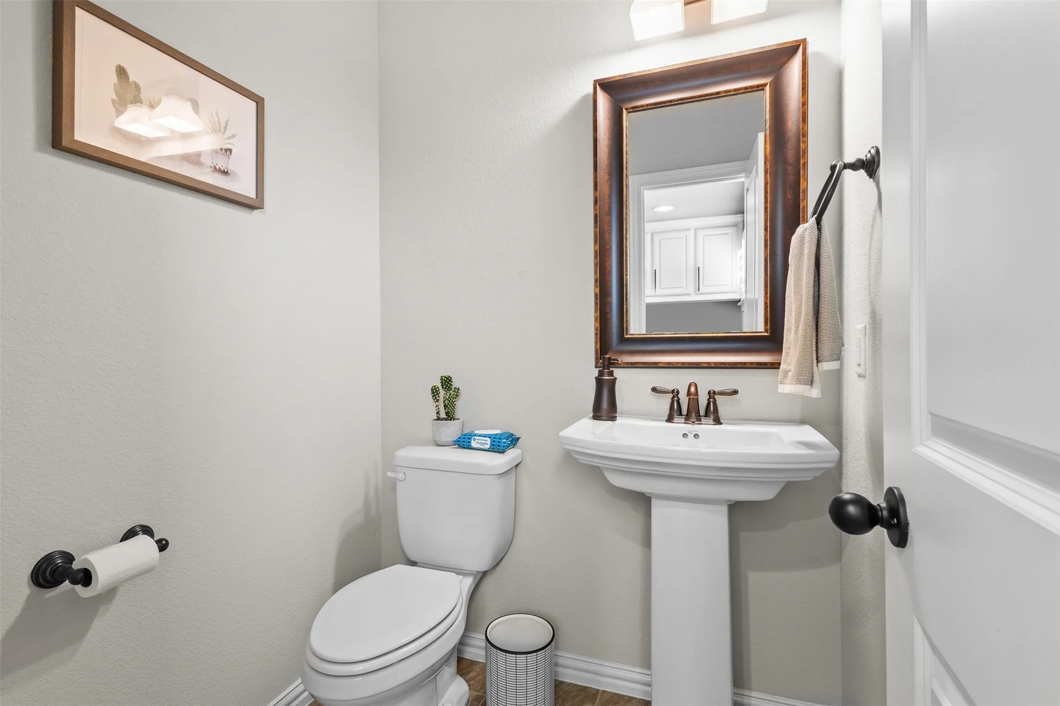 Pedestal sink with bronze-tone faucet set under a framed mirror