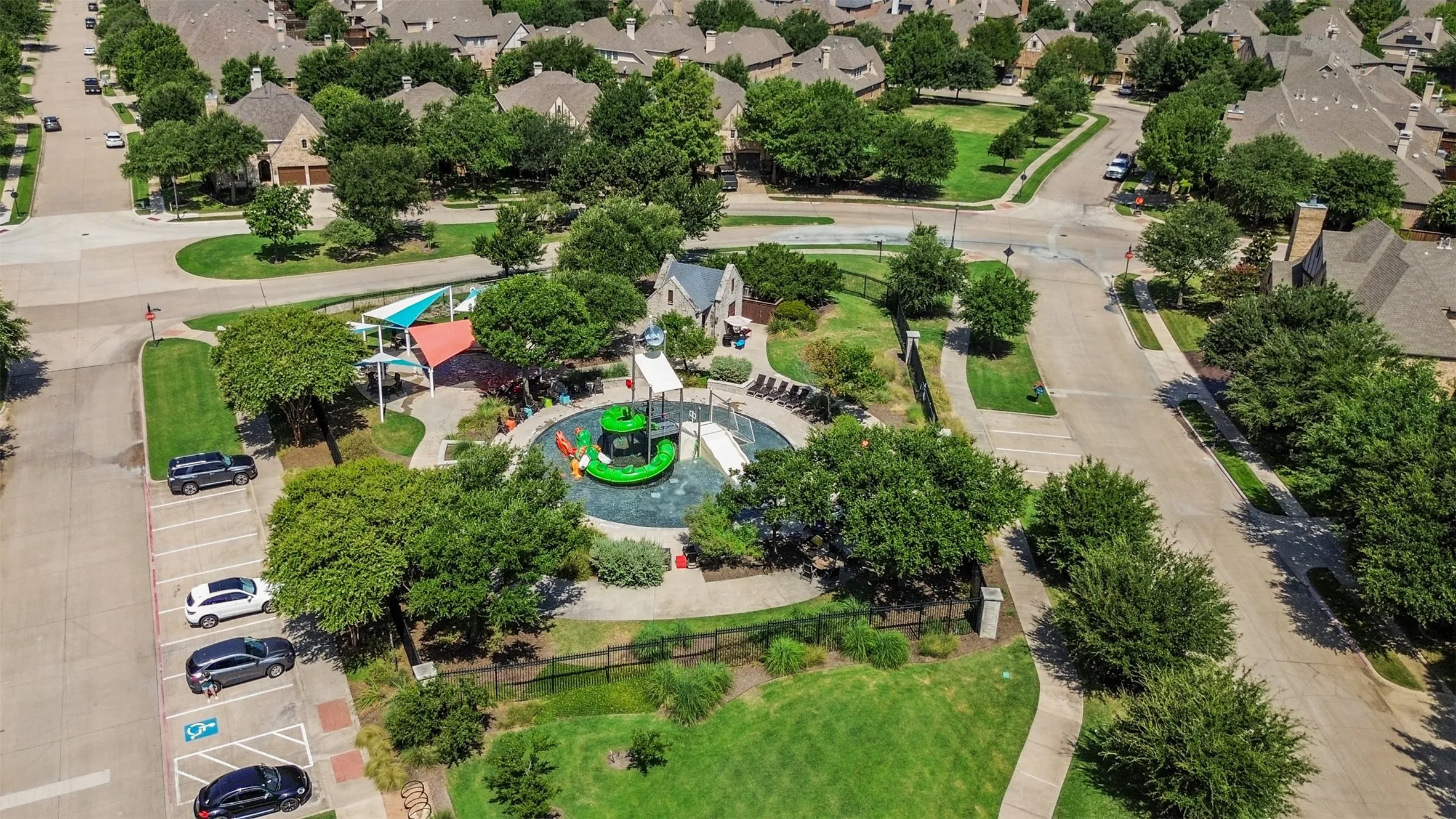 Community splash pad featuring multiple slides, shaded lounge areas, and surrounding green spaces