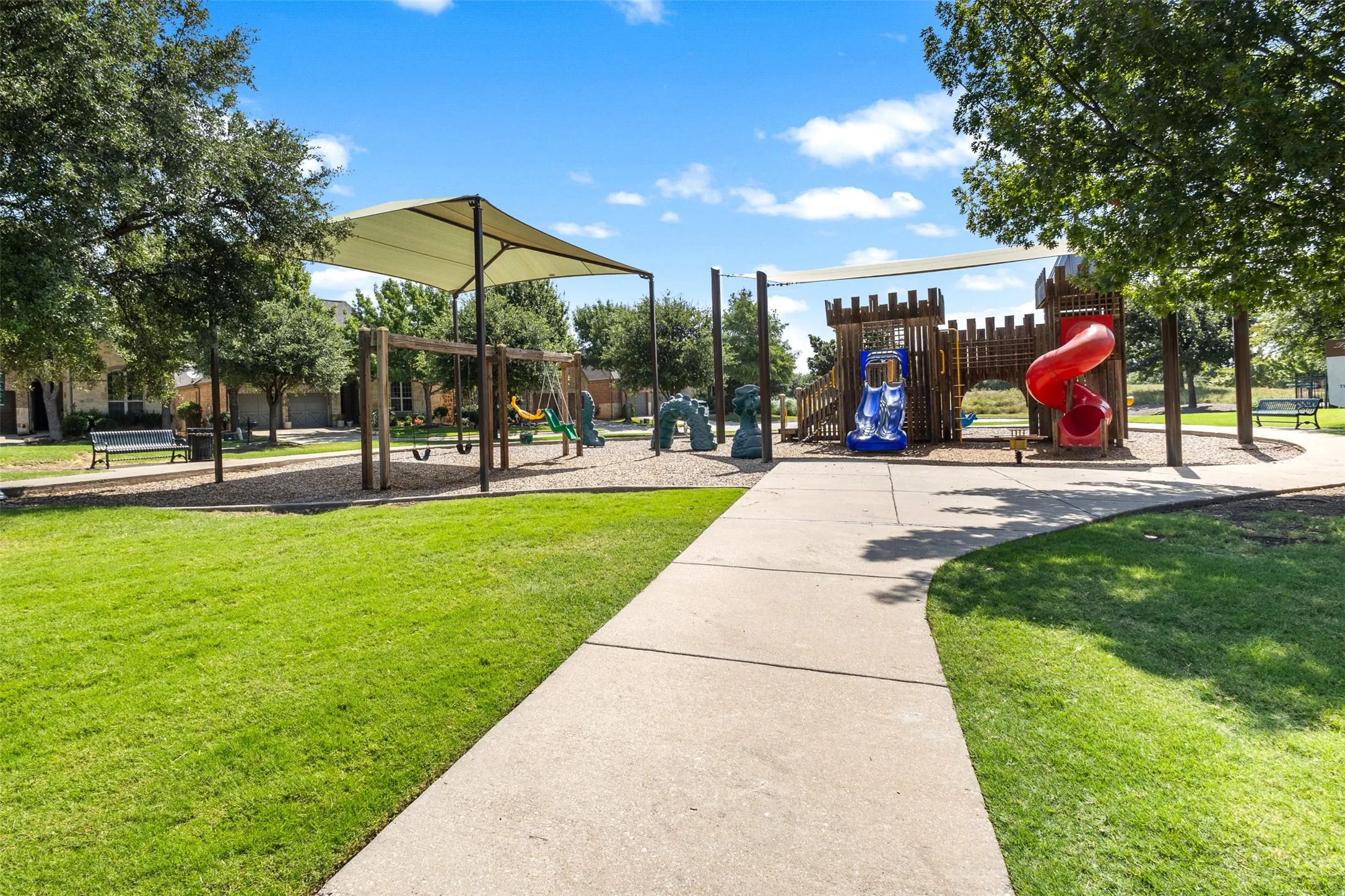 Community playground area featuring a castle-themed play structure with a red slide, a swing set, and a shaded canopy