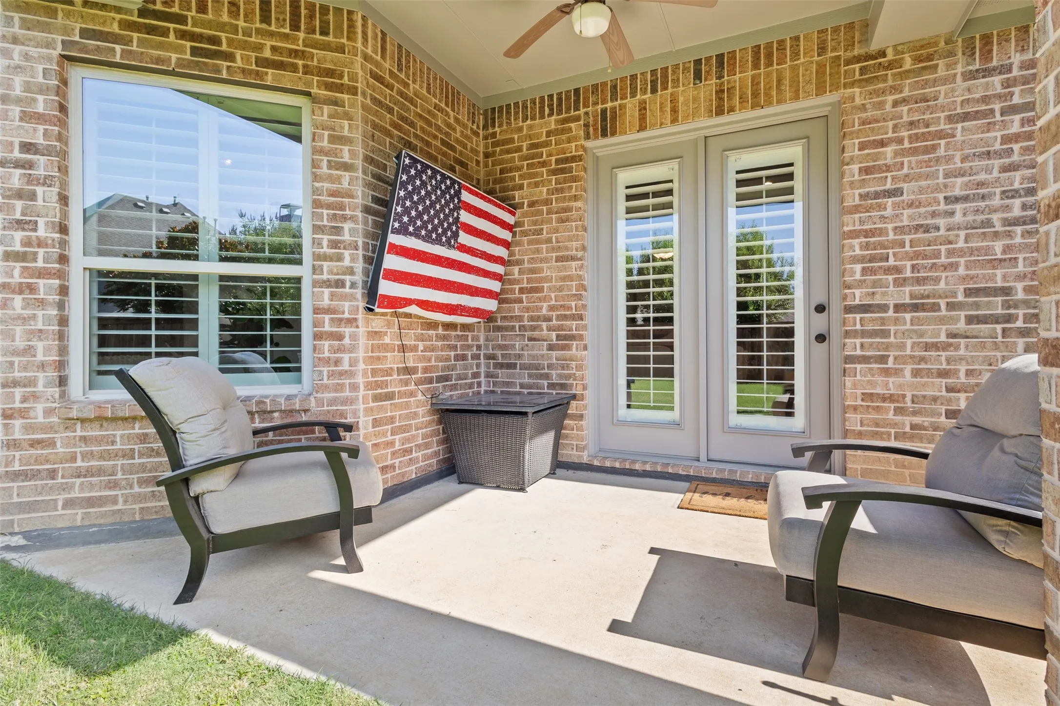 Covered patio featuring a ceiling fan, dual French doors with interior blinds, brick exterior, and an adjacent window with interior blinds