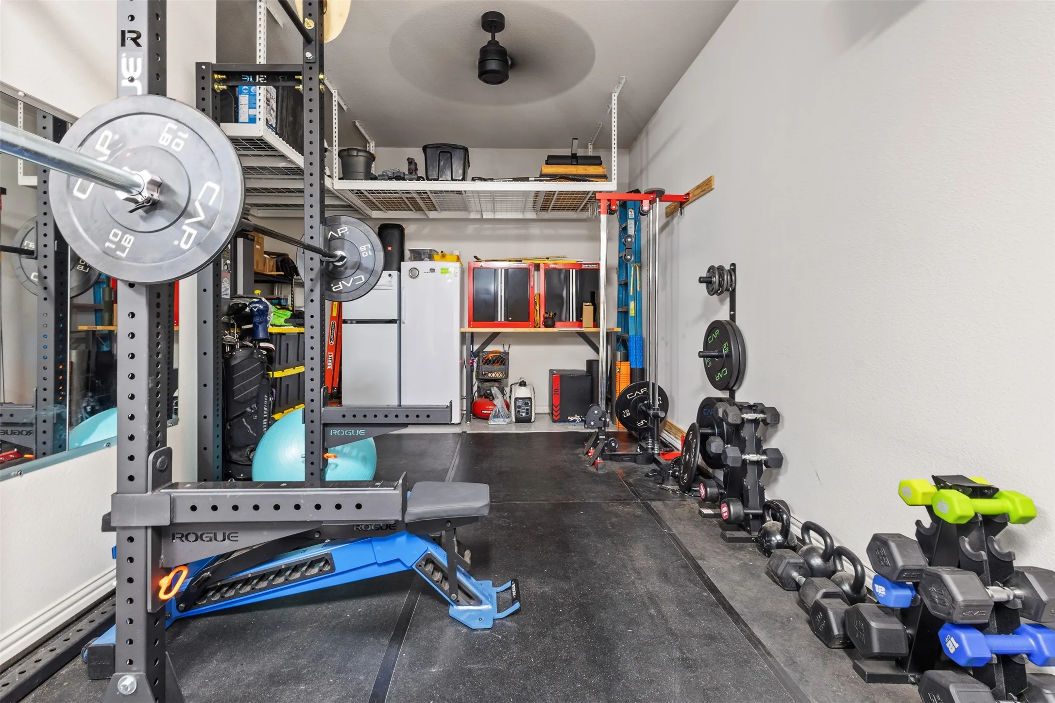 Dedicated fitness area featuring rubber flooring, extensive metal shelving, ceiling-mounted fan, and wall-mounted mirror