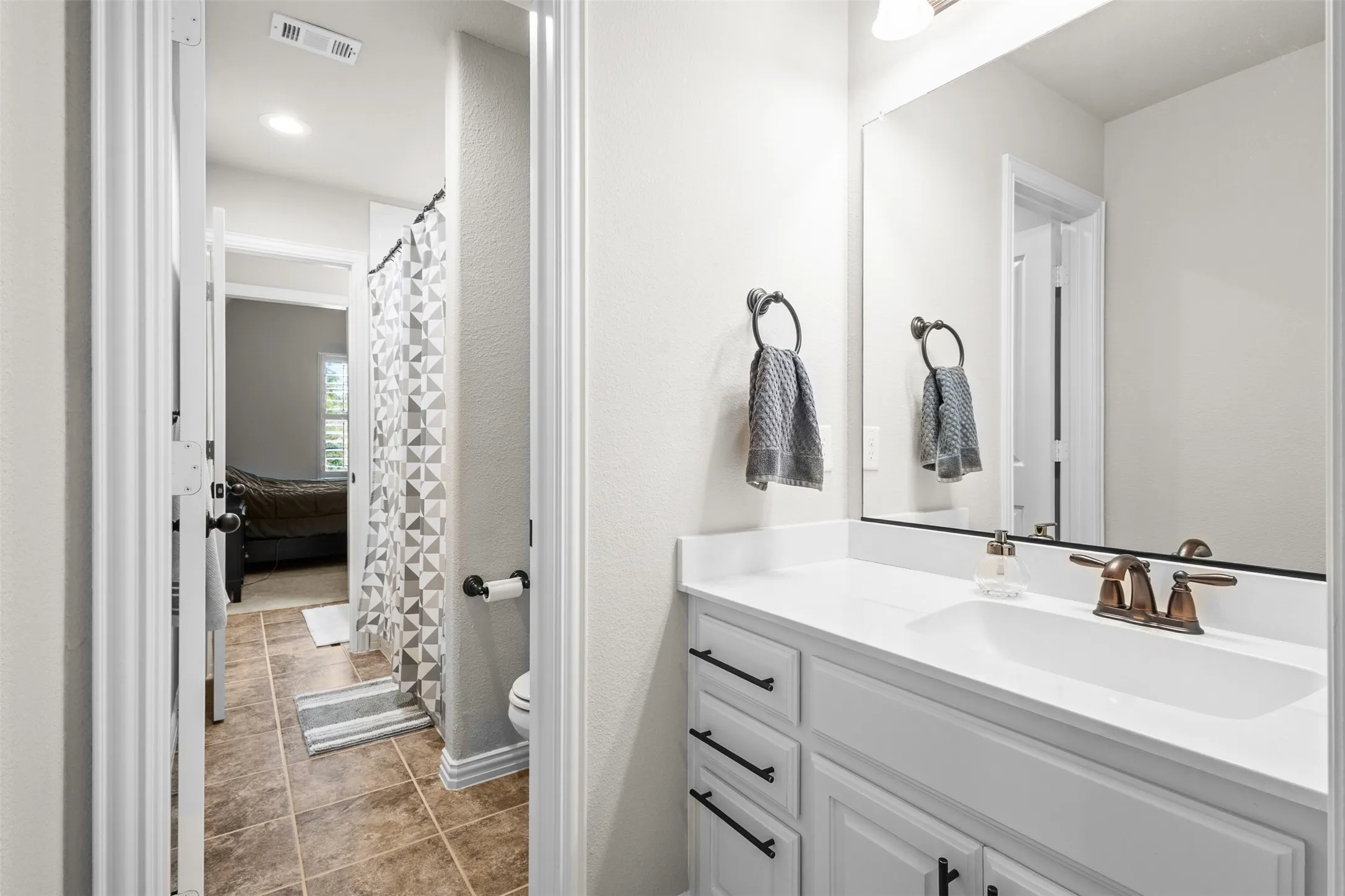 Bathroom vanity with a white countertop and integrated sink, featuring a bronze-finish faucet, a large wall-mounted mirror, and white cabinetry with black pulls