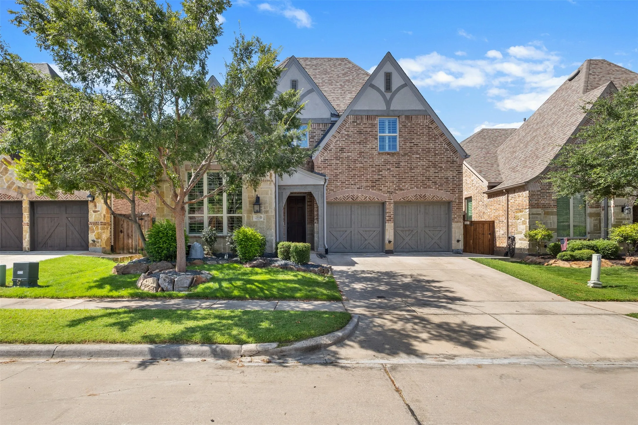 Traditional-style home showcasing a brick and stone facade, a multi-gabled roofline, and a two-car garage with carriage-style doors