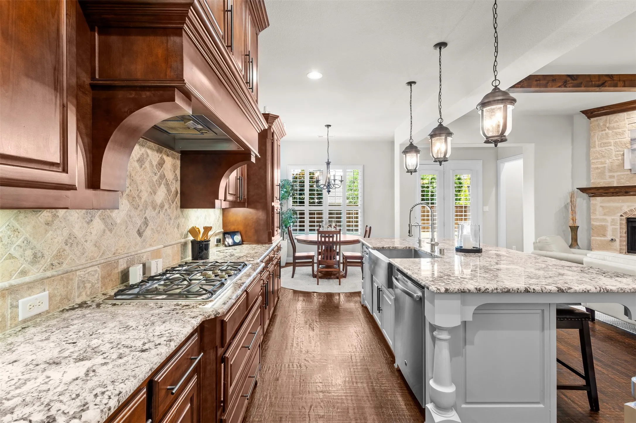 Gourmet kitchen featuring a gas range cooktop, granite countertops, wood-finish flooring, a farmhouse sink, and custom cabinetry with an integrated vent hood