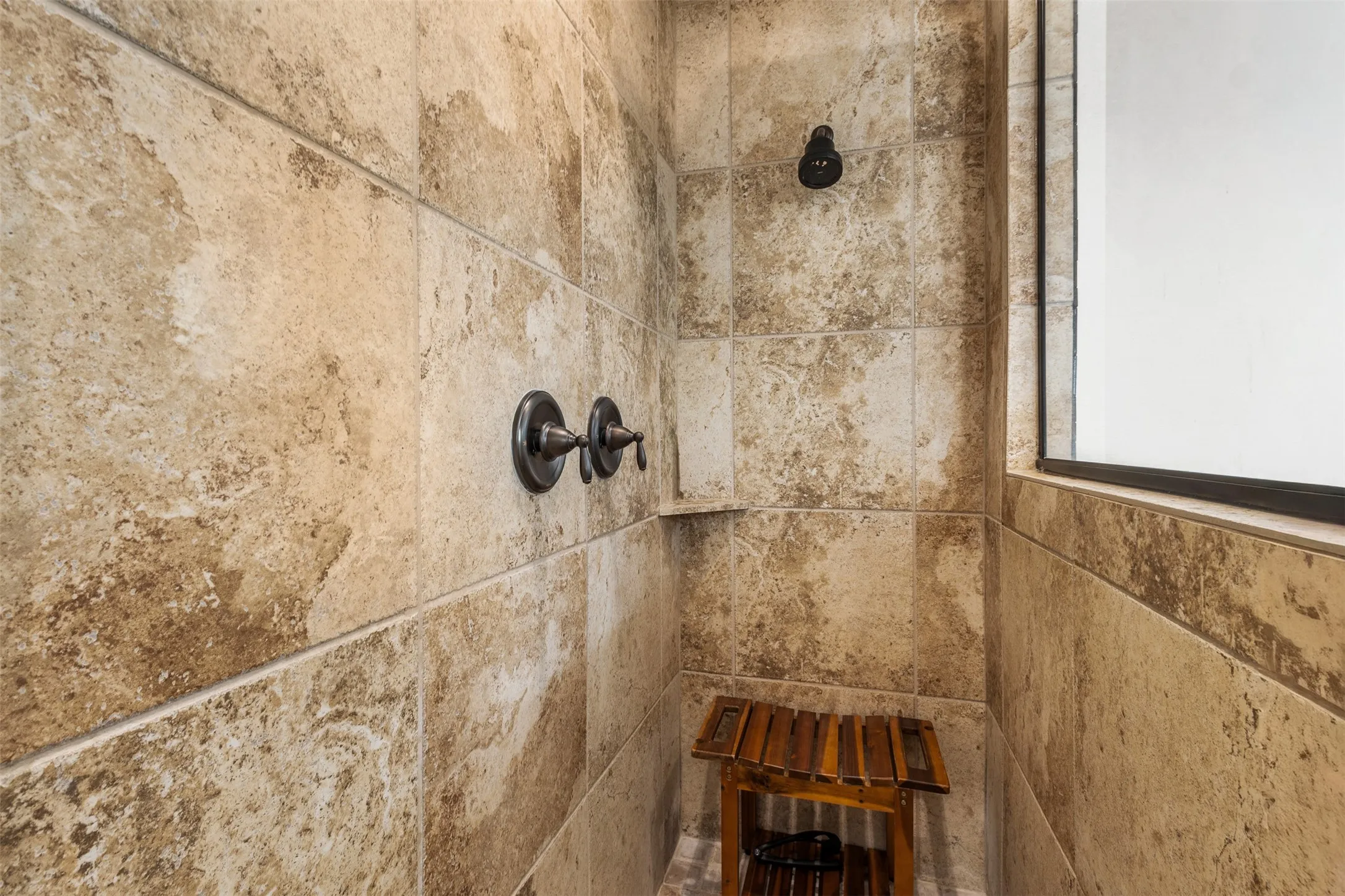 Tiled shower enclosure featuring a fixed showerhead, separate control knobs, and a built-in ledge