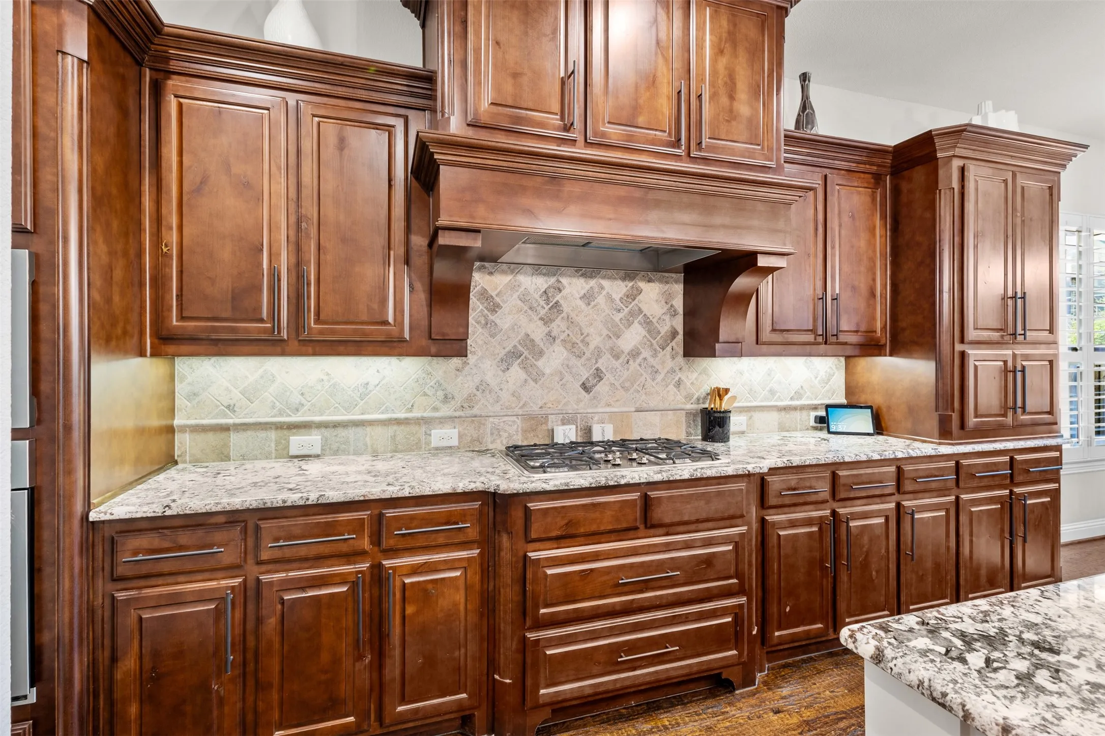 Kitchen featuring rich wood cabinetry, stone countertops, a gas cooktop, and a herringbone-patterned tile backsplash