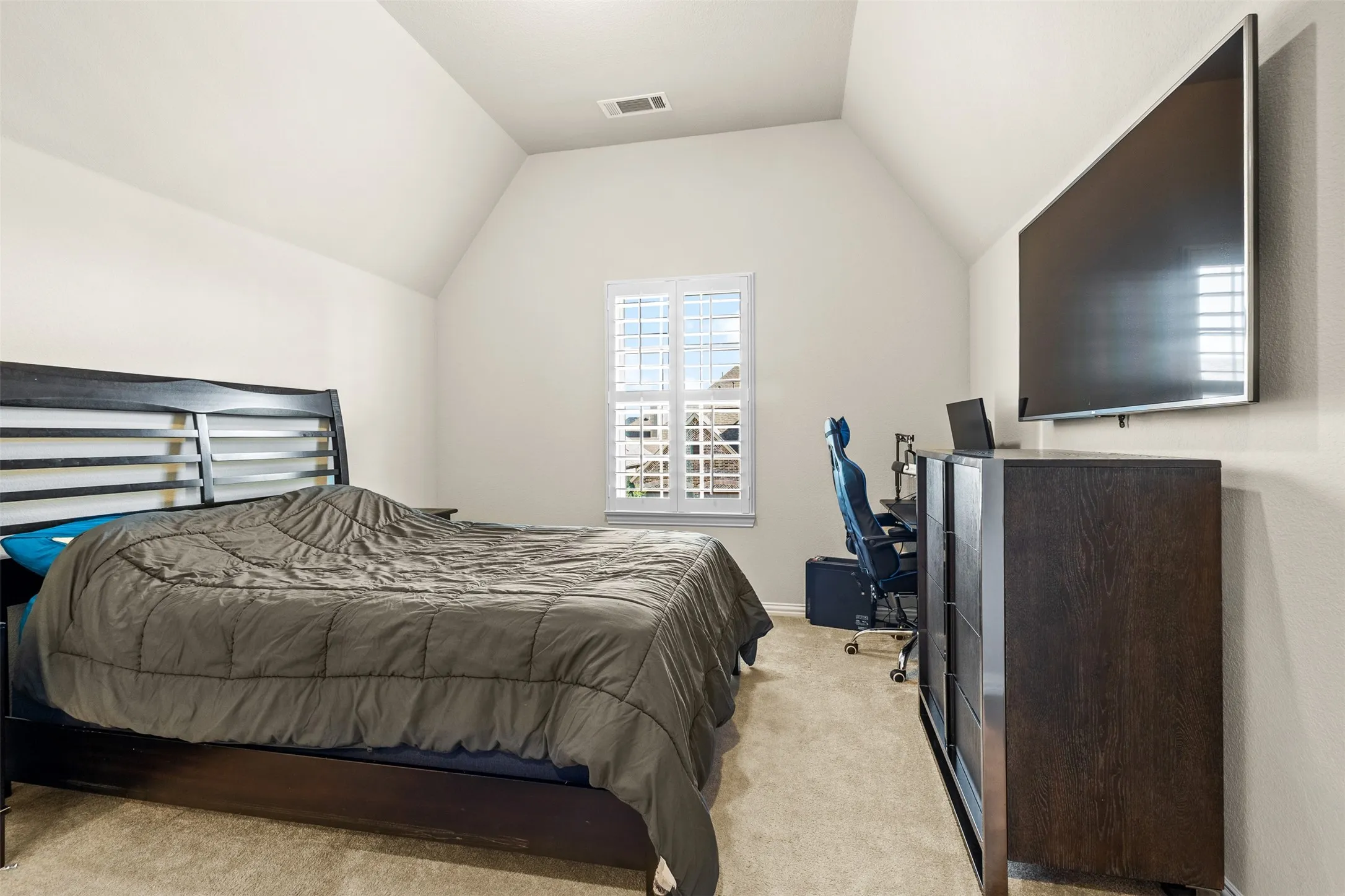 Carpeted room featuring a vaulted ceiling and a window with white louvered shutters