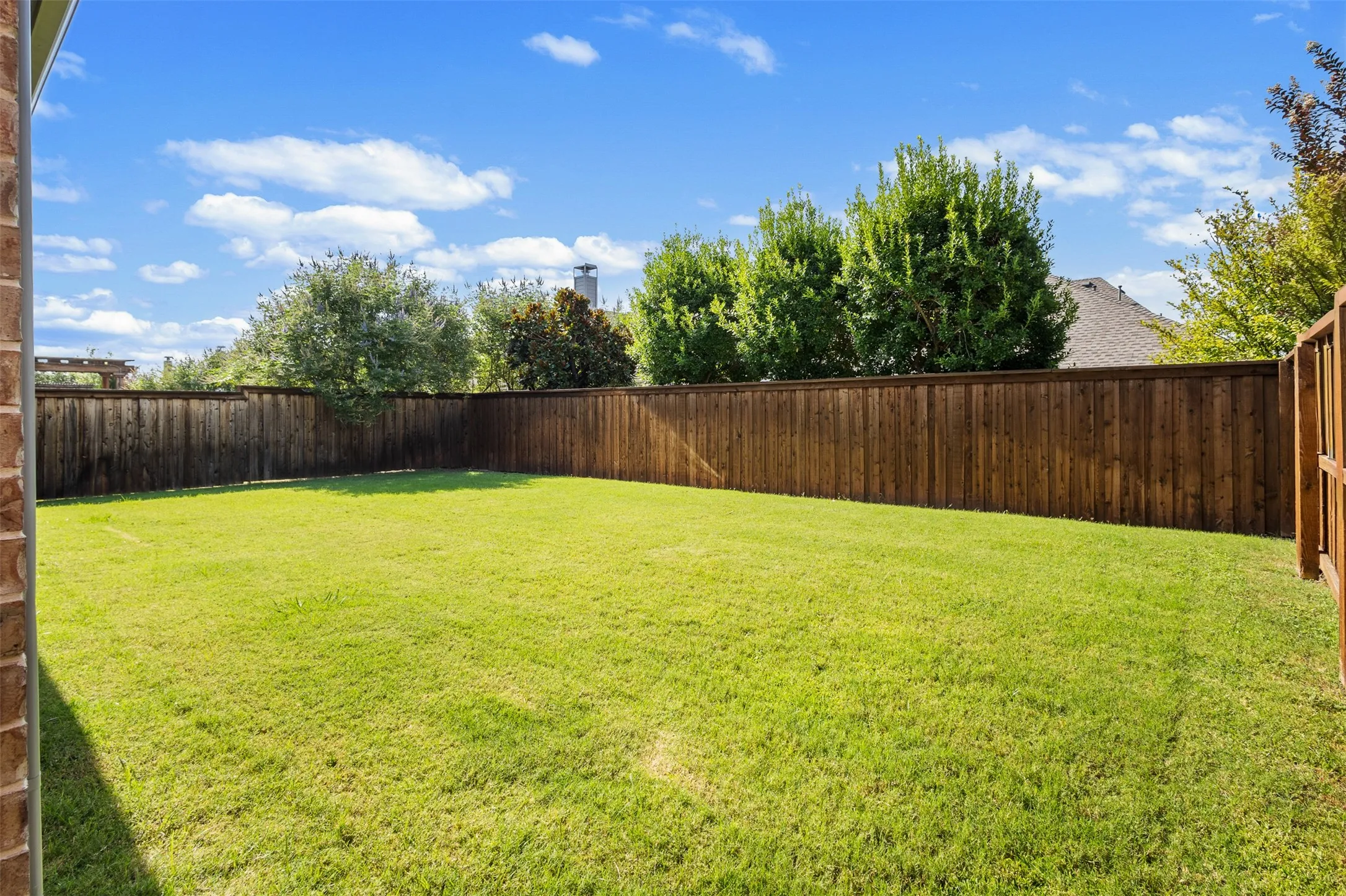 Expansive backyard featuring a manicured lawn, a full-height privacy fence, and mature perimeter trees