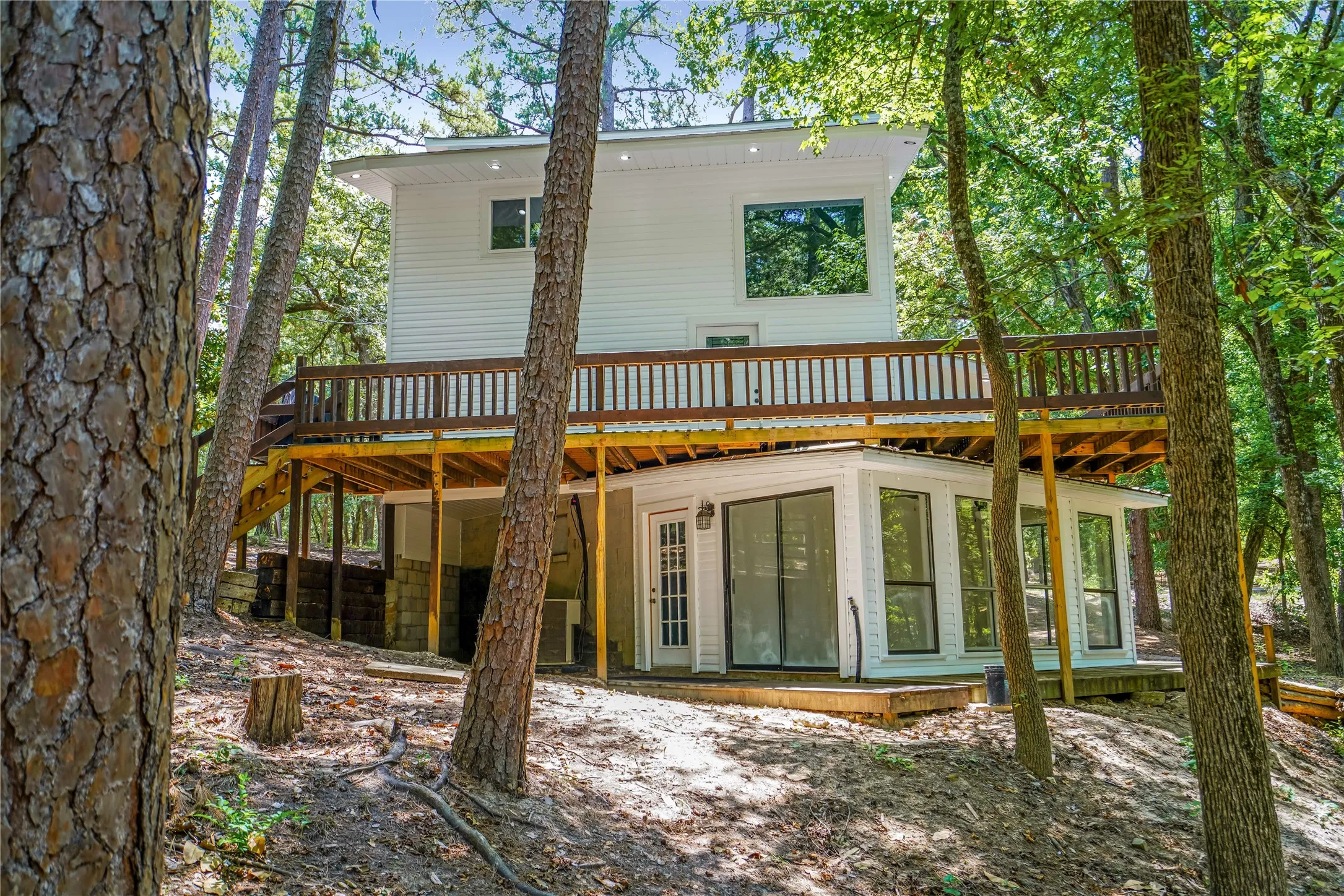Multi-level residence featuring white siding and extensive wood decking, surrounded by mature trees