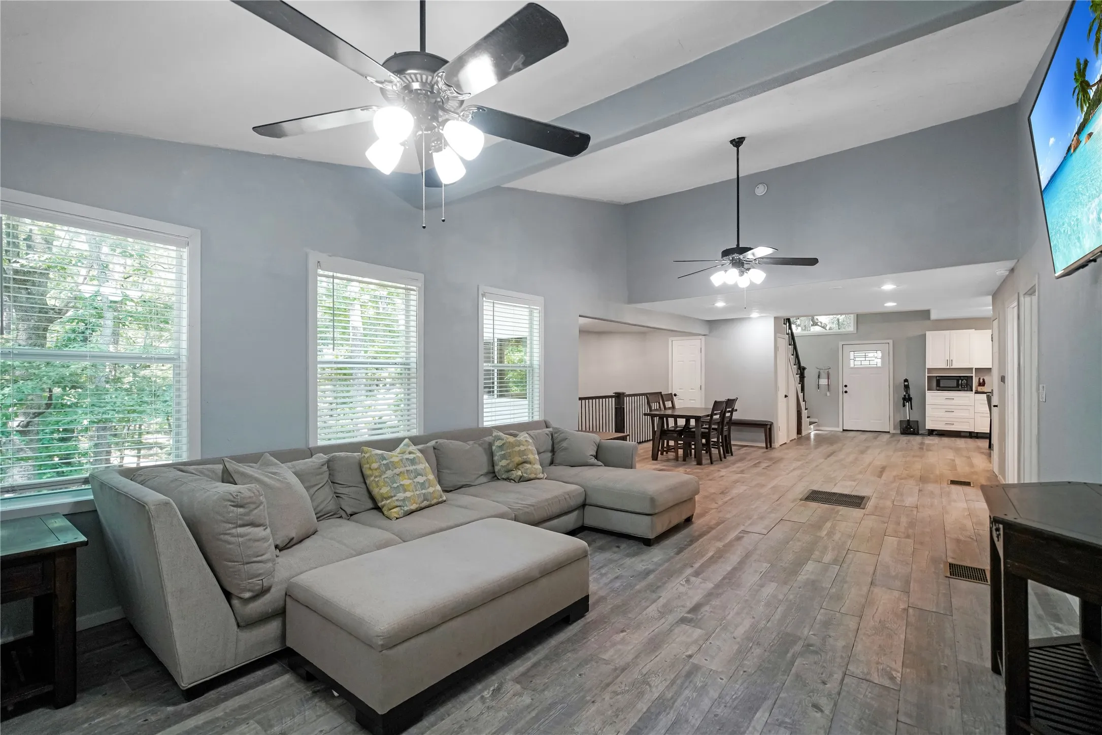 Spacious open-concept living area featuring vaulted ceilings, wood-finish flooring, multiple ceiling fans, and abundant natural light from numerous windows
