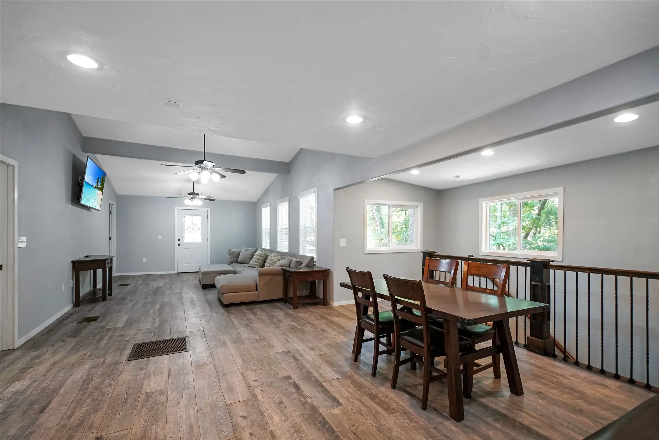 Spacious open-concept living area featuring vaulted ceilings with exposed beams, wood-finish flooring, recessed lighting, and multiple windows