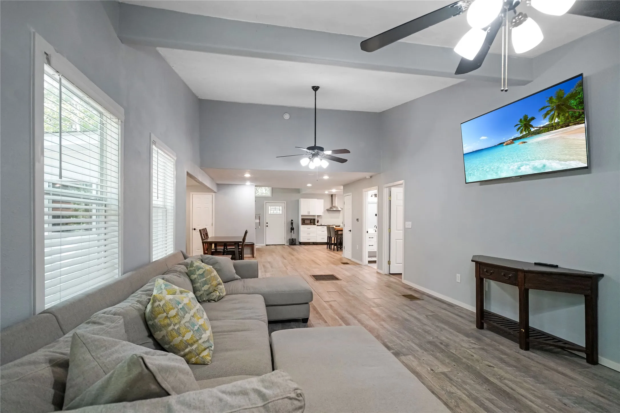 Spacious living area featuring vaulted ceilings with exposed beams, wood-finish flooring, and multiple windows with blinds