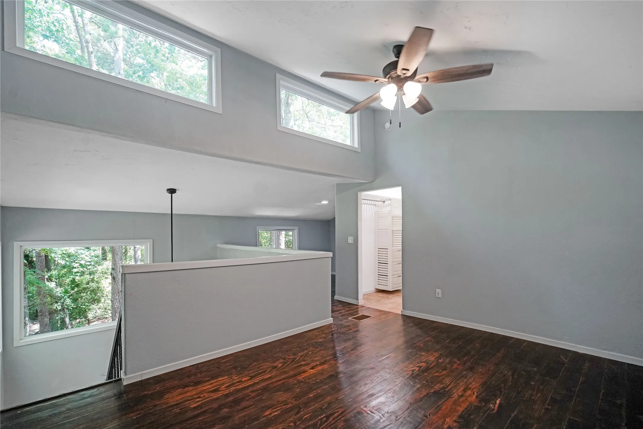 Expansive interior space featuring wood-finish flooring, a ceiling fan with integrated lighting, and multiple windows