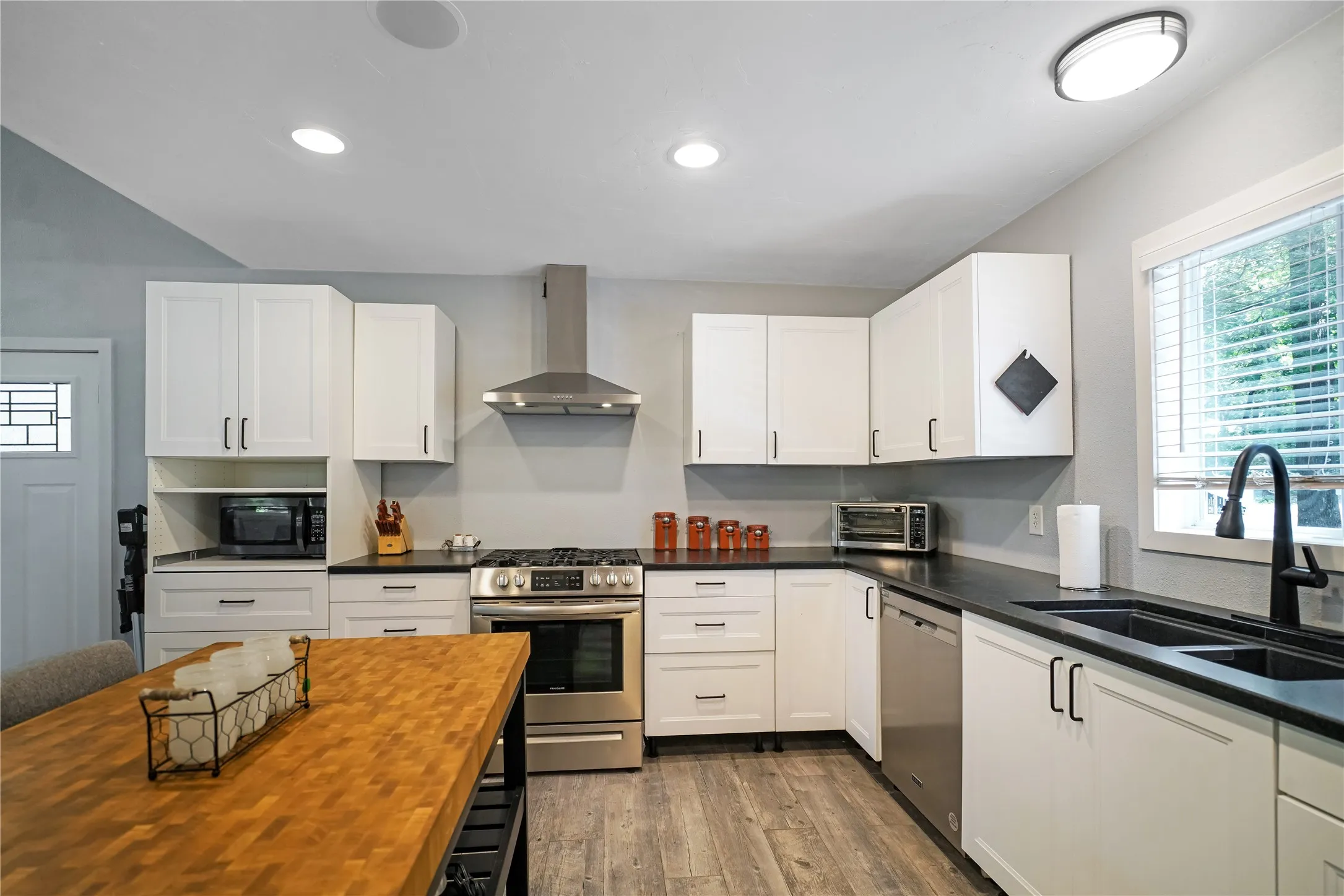 Kitchen featuring white shaker-style cabinetry, dark countertops, stainless steel appliances, wood-finish flooring, and recessed lighting
