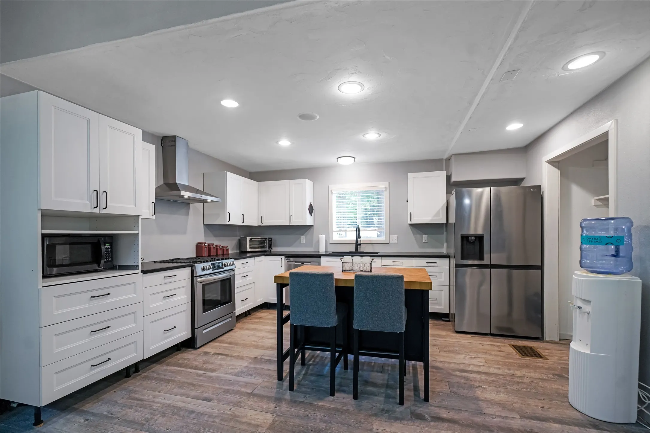 Kitchen featuring white cabinetry, stainless steel appliances, black countertops, a central island with wood countertop, and wood-finish flooring