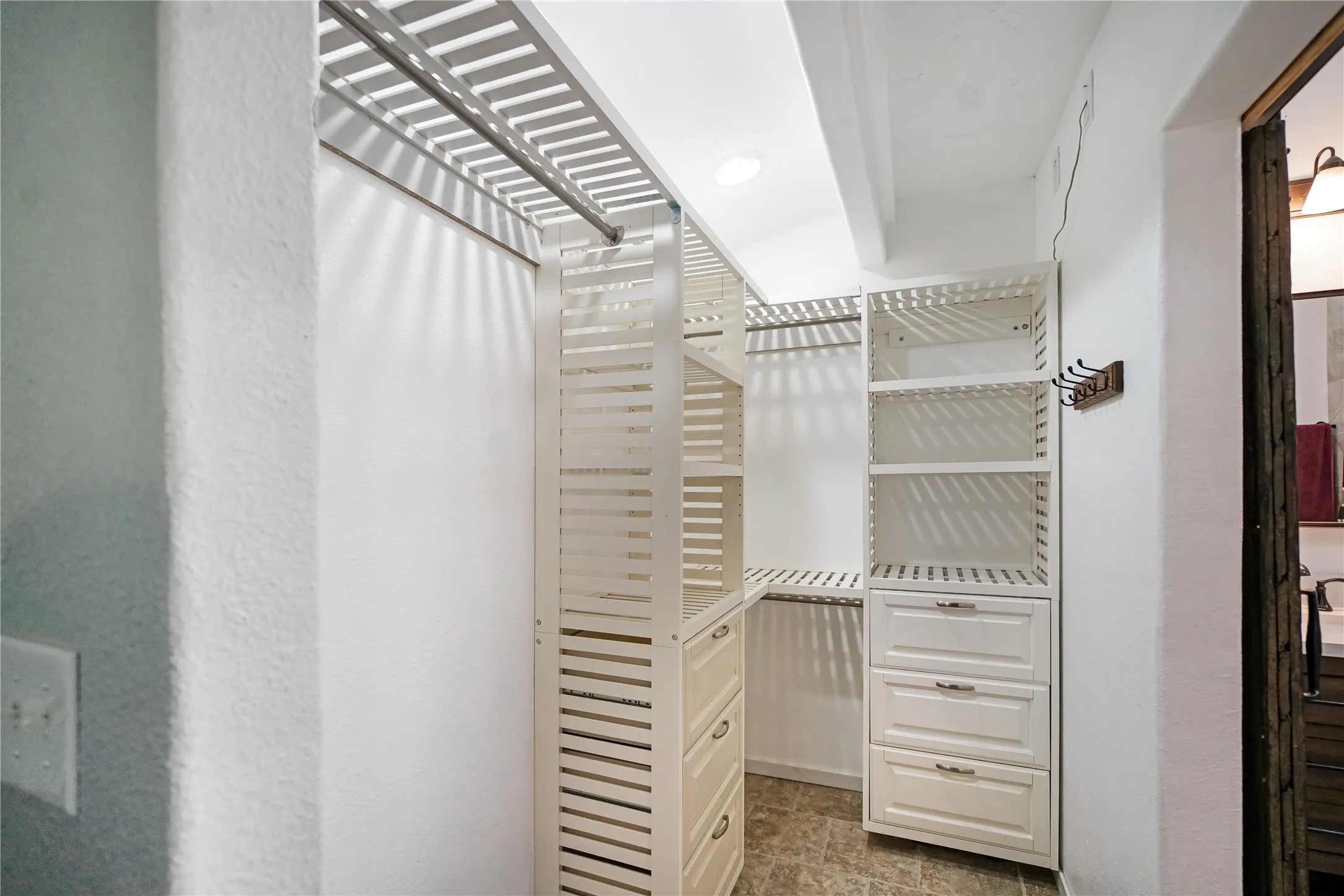 Walk-in closet featuring white built-in shelving, multiple hanging rods, and integrated drawer storage