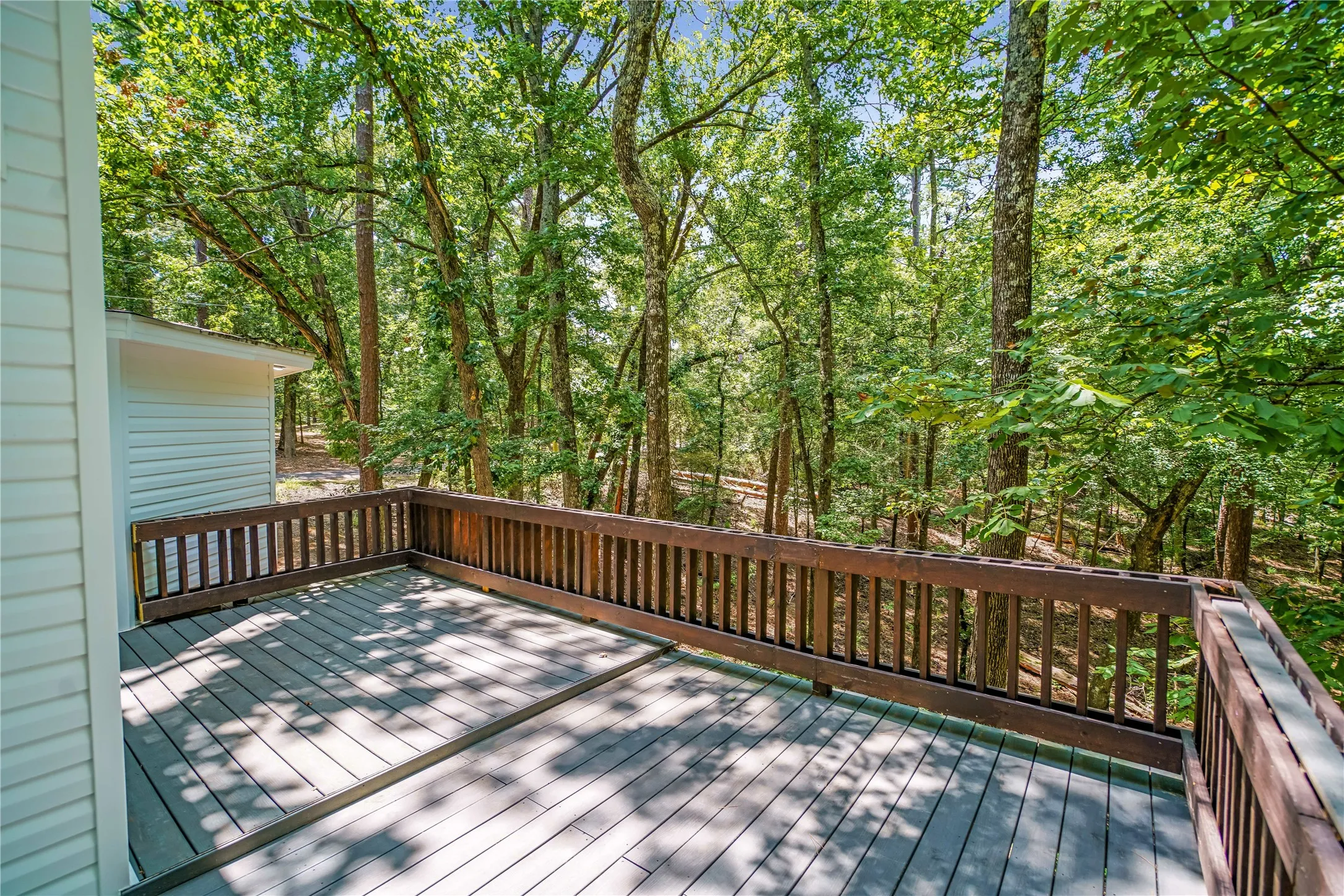 Spacious deck featuring composite decking, wood railings, and a densely treed backdrop