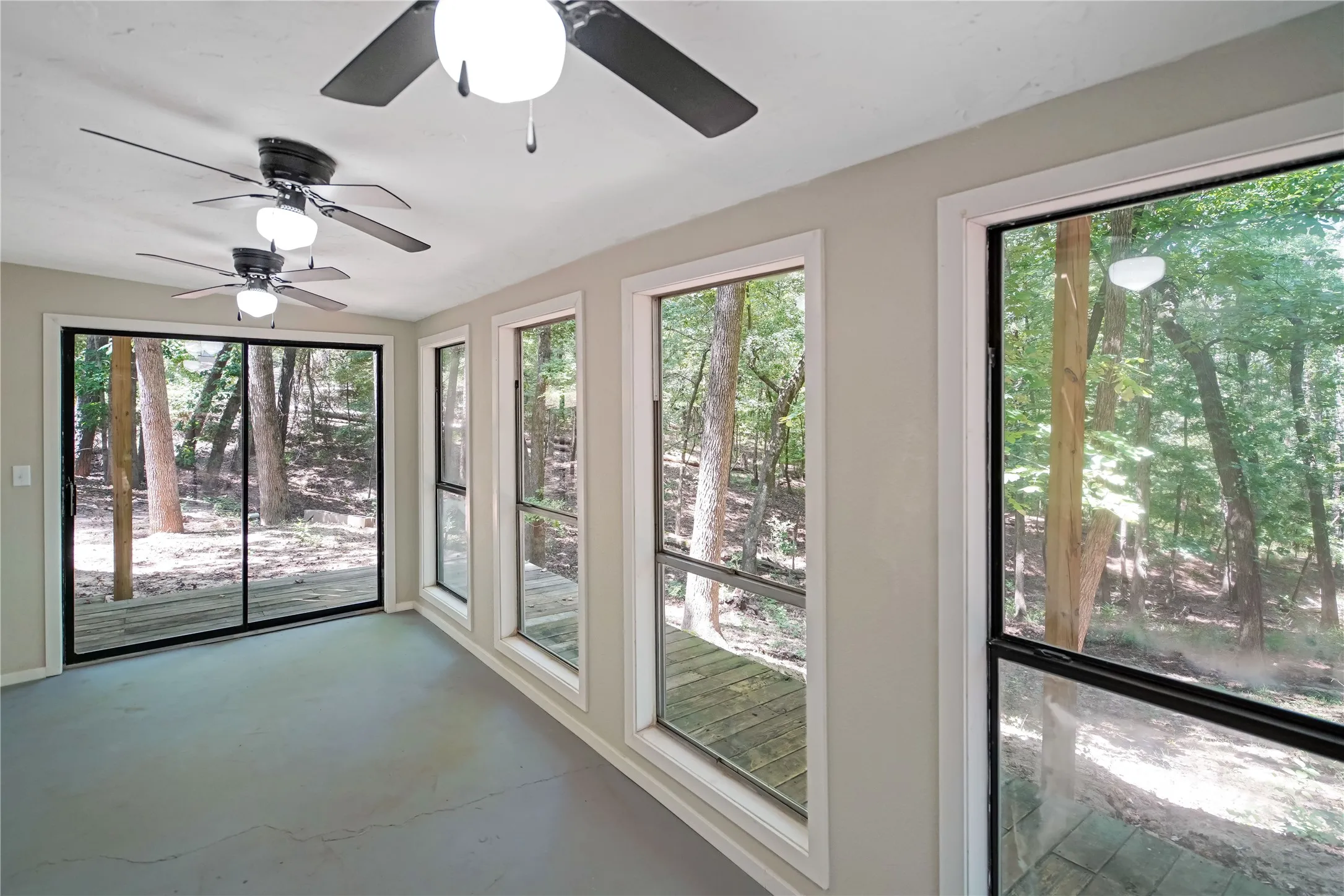 Sunroom featuring multiple ceiling fans, a full wall of windows, a sliding glass door, and exterior wooden deck