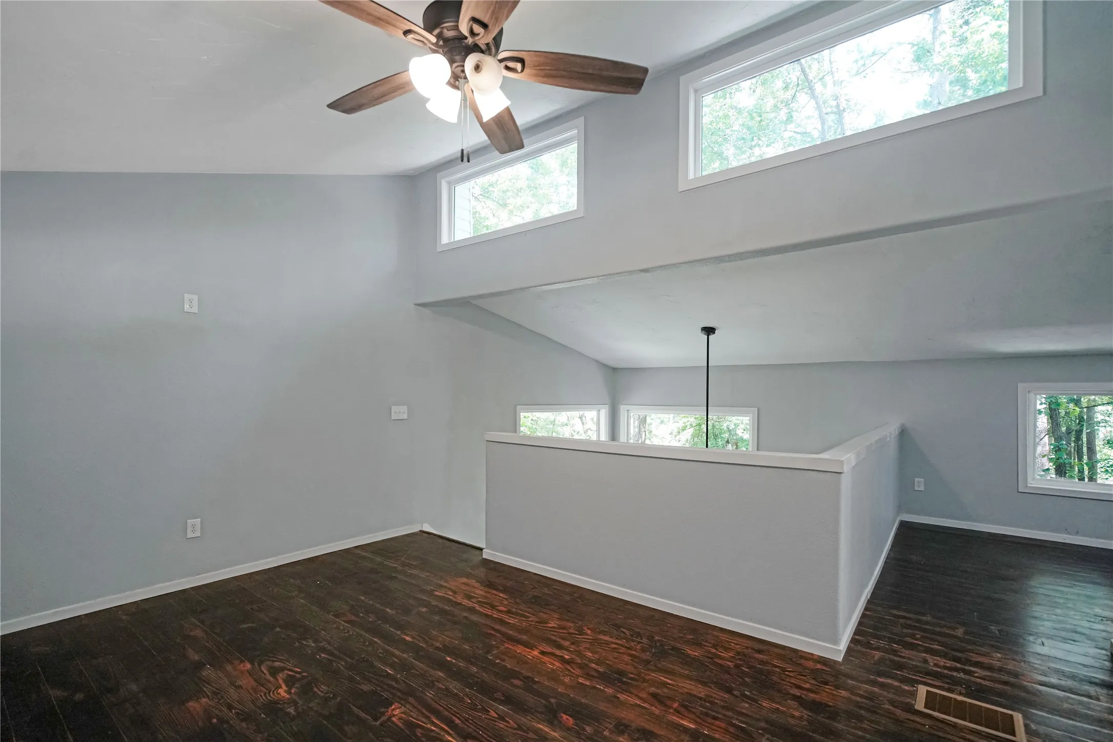 Vaulted ceilings with a ceiling fan, wood-finish flooring, high transom windows, and a partial wall with a​​‌​​​​‌​​‌‌​‌‌​​​‌‌​‌​‌​‌​​​‌​​ railing