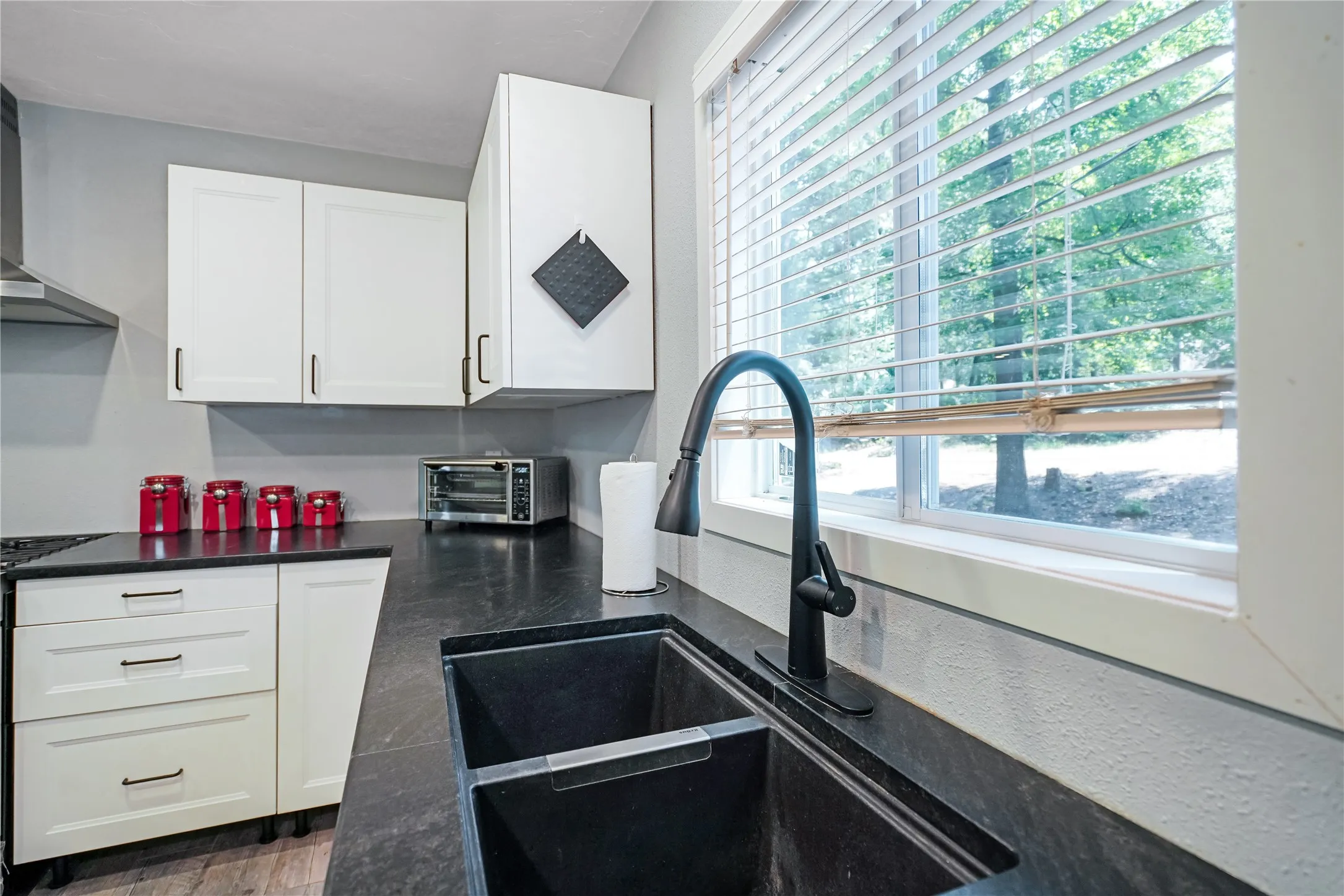 Kitchen featuring white cabinetry with black hardware, dark countertops, a dual basin sink with a matte black high-arc faucet, and wood-finish flooring
