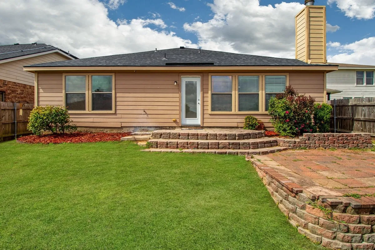 Backyard featuring a paver patio with a stone block retaining wall, a green lawn, and shrubbery
