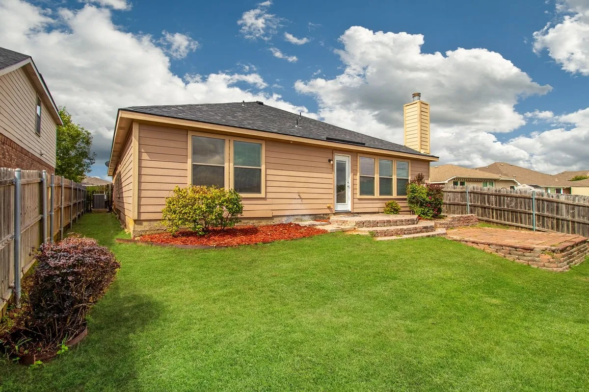 Spacious backyard featuring a manicured lawn, a two-tier brick paver patio, wood siding, and multiple windows