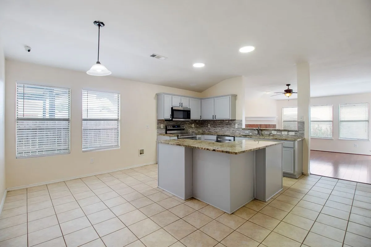 Kitchen featuring an island with a light-toned countertop, gray cabinetry, tile backsplash, and stainless steel microwave