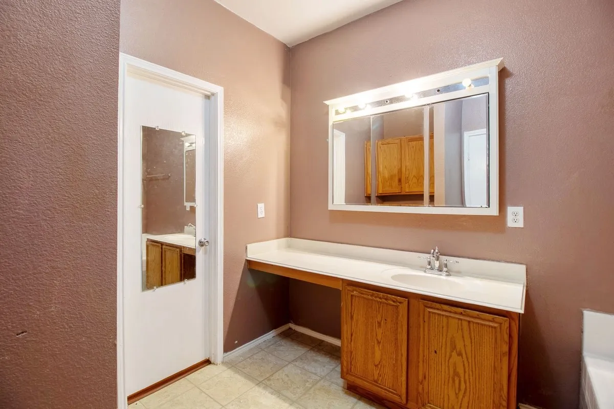 Vanity area with a single basin sink, laminate countertop, wood-finish cabinetry, and a mirrored medicine cabinet with integrated lighting