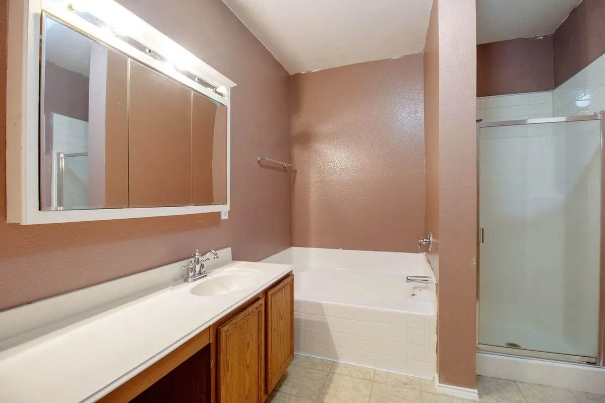 Bathroom featuring a dual-sink vanity with white countertop, wood-finish cabinetry, and a mirrored medicine cabinet with integrated lighting