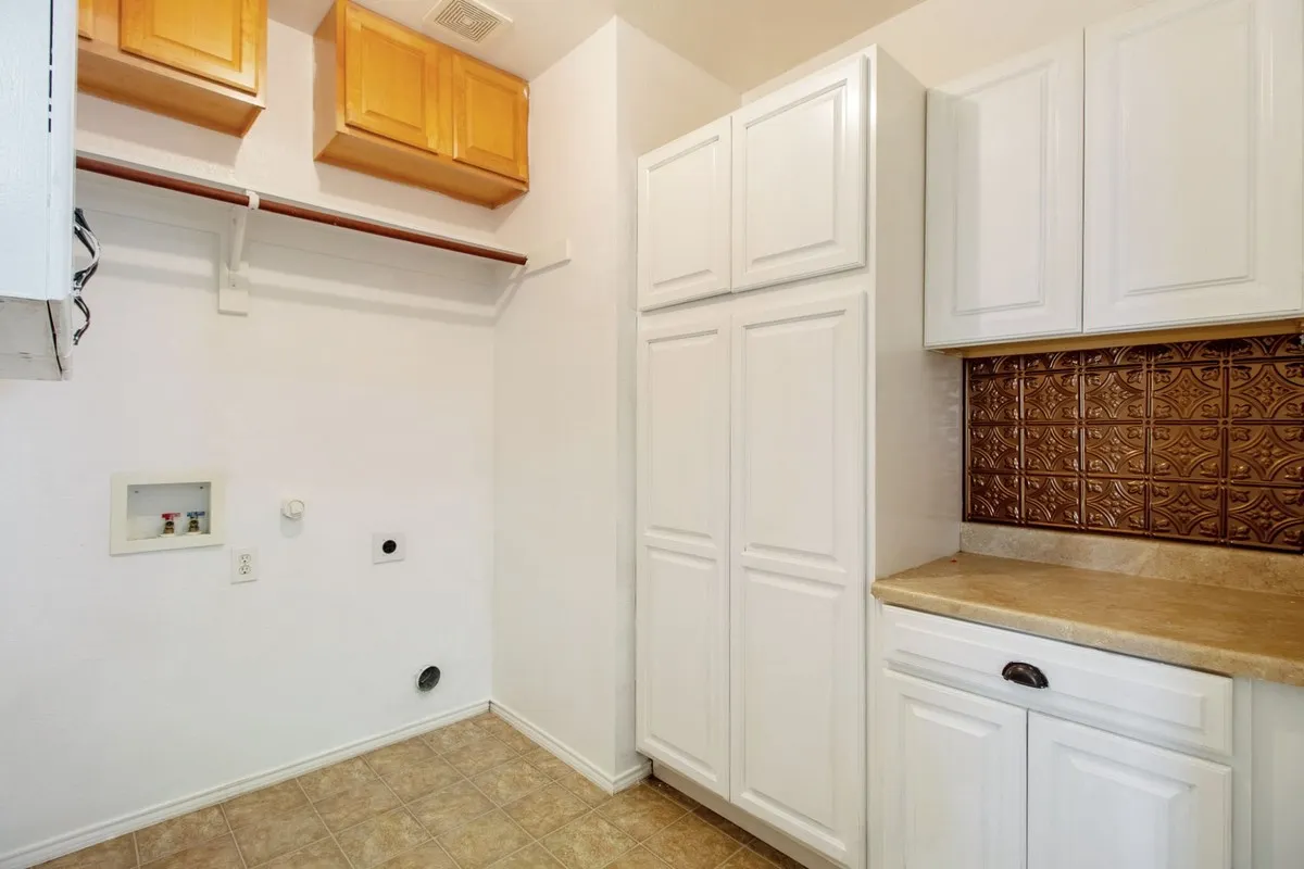 Dedicated laundry area featuring white cabinetry, a built-in folding counter, and a decorative copper-toned backsplash