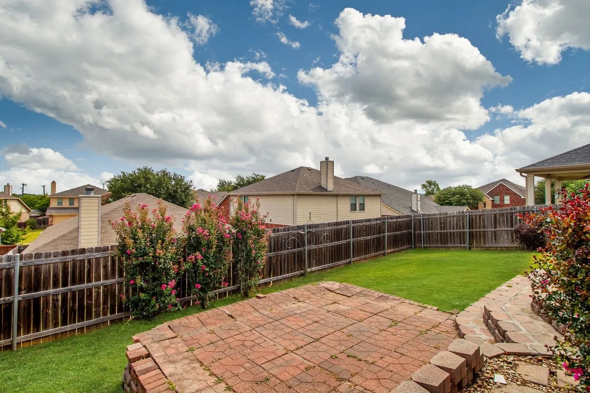 Expansive green lawn featuring a brick paver patio and mature flowering shrubs